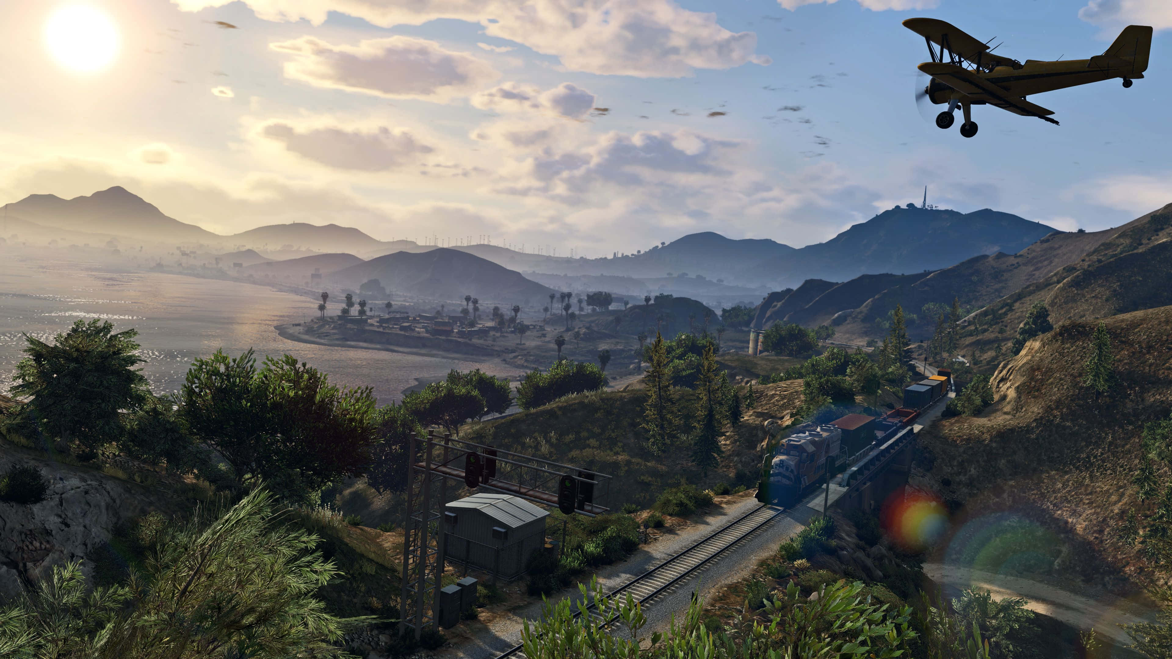 Gta V 4K 桌布 壁紙 — 一架雙翼飛機飛越陽光明媚的山谷，一列火車沿著軌道穿過鬱鬱蔥蔥的綠色山丘。