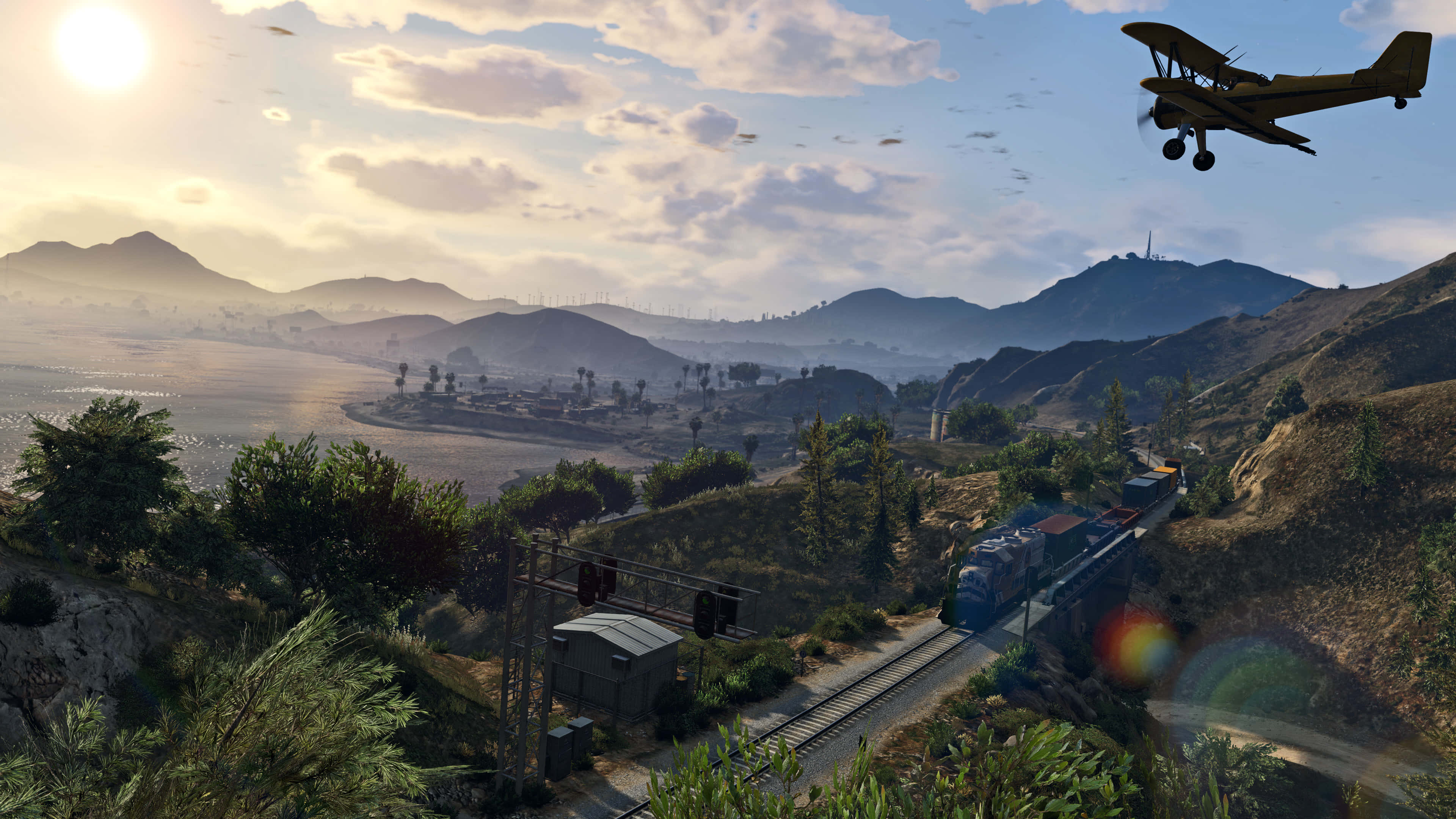 Gta 5 4K 桌布 壁紙 — 一架雙翼飛機飛越陽光照耀的山谷，一列火車沿著軌道穿過起伏的丘陵和散落的樹木。