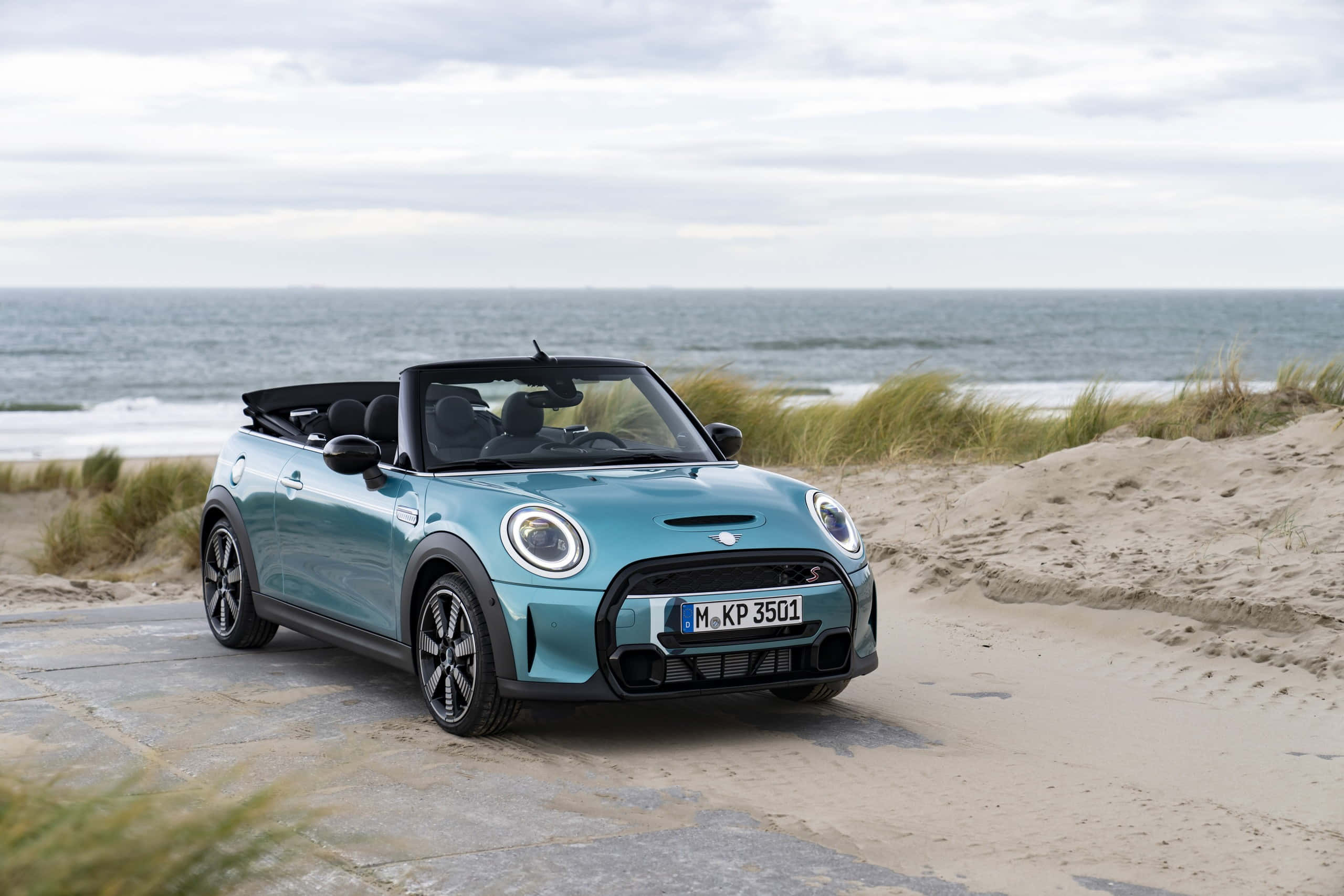 Mini Cooper Convertible 桌布 壁紙 — 一架青綠色MINI敞篷車停泊在海岸小徑上，背景有海浪和沙丘，天空多雲。