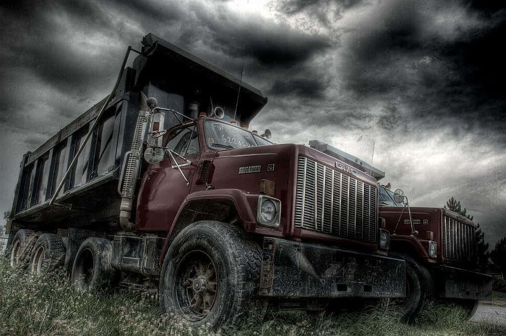 Jacked Up Trucks 桌布 壁紙 — 一架風化的栗色傾卸車被遺棄在草地上，天空是戲劇性的暴風雨，佈滿烏雲。