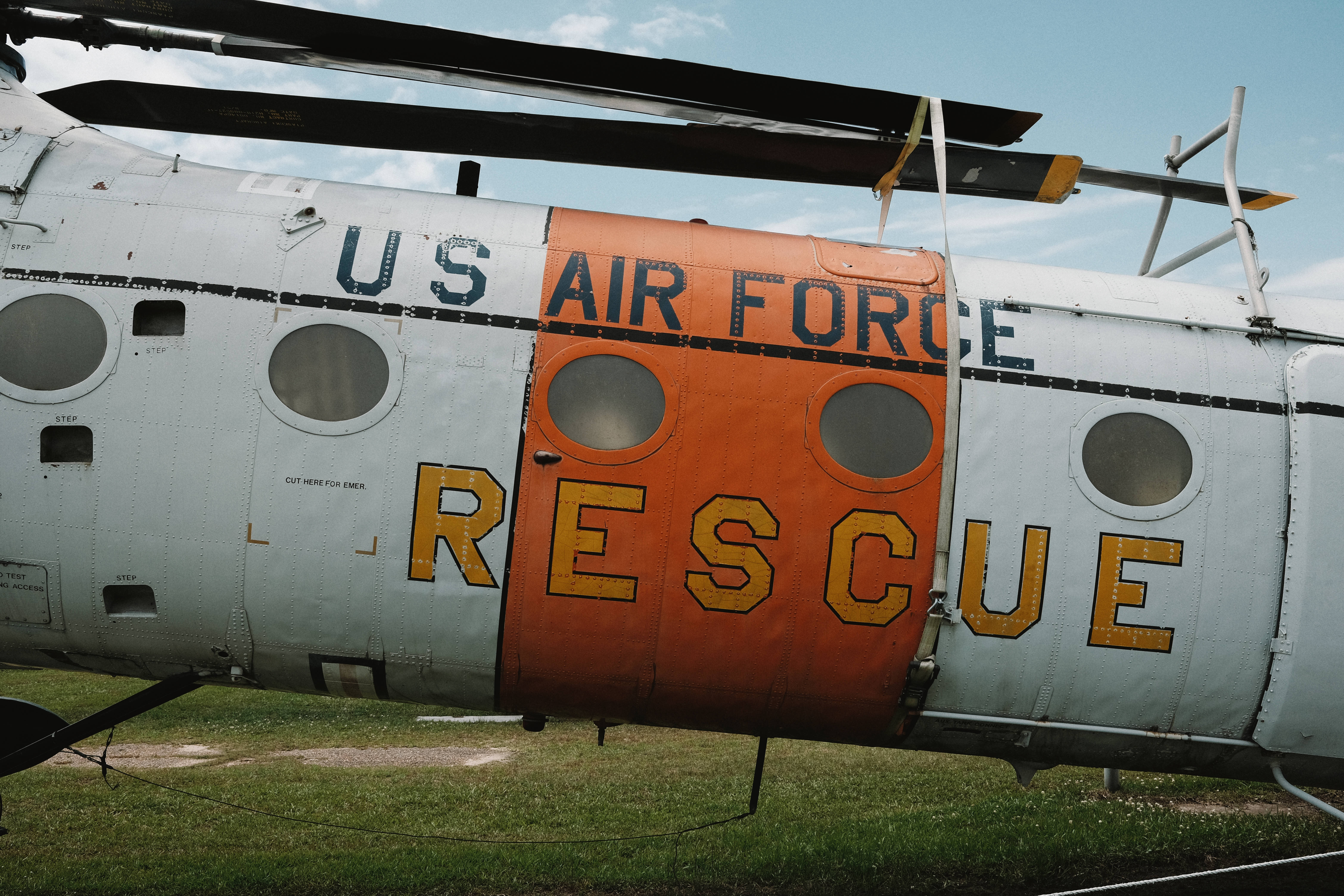 Air Force 桌布 壁紙 — 一架風化的美國空軍救援直升機停在草地上，天空局部多雲，有醒目的橙色和白色標記。