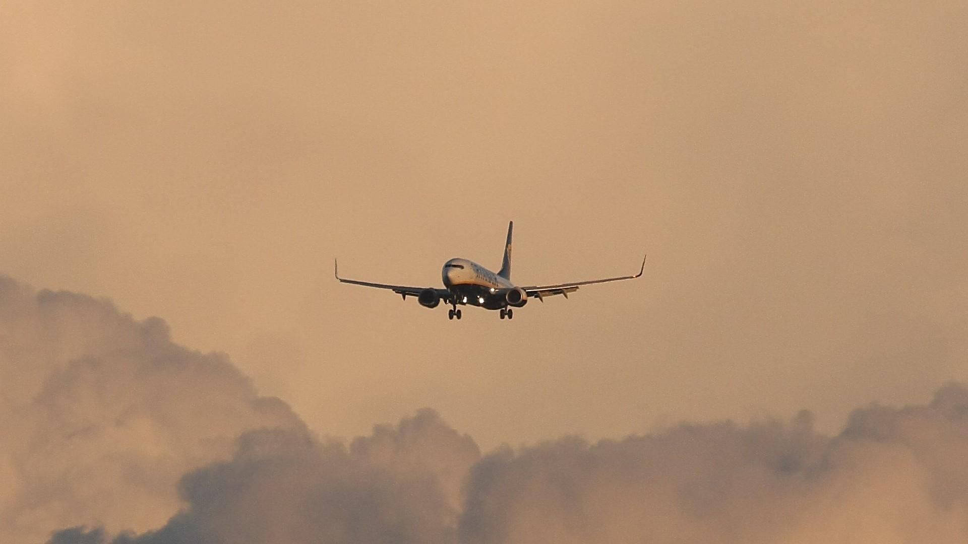 飛機 桌布 壁紙 — 一架飛機在日落時分穿過朦朧的橙色雲層下降，起落架已放下。