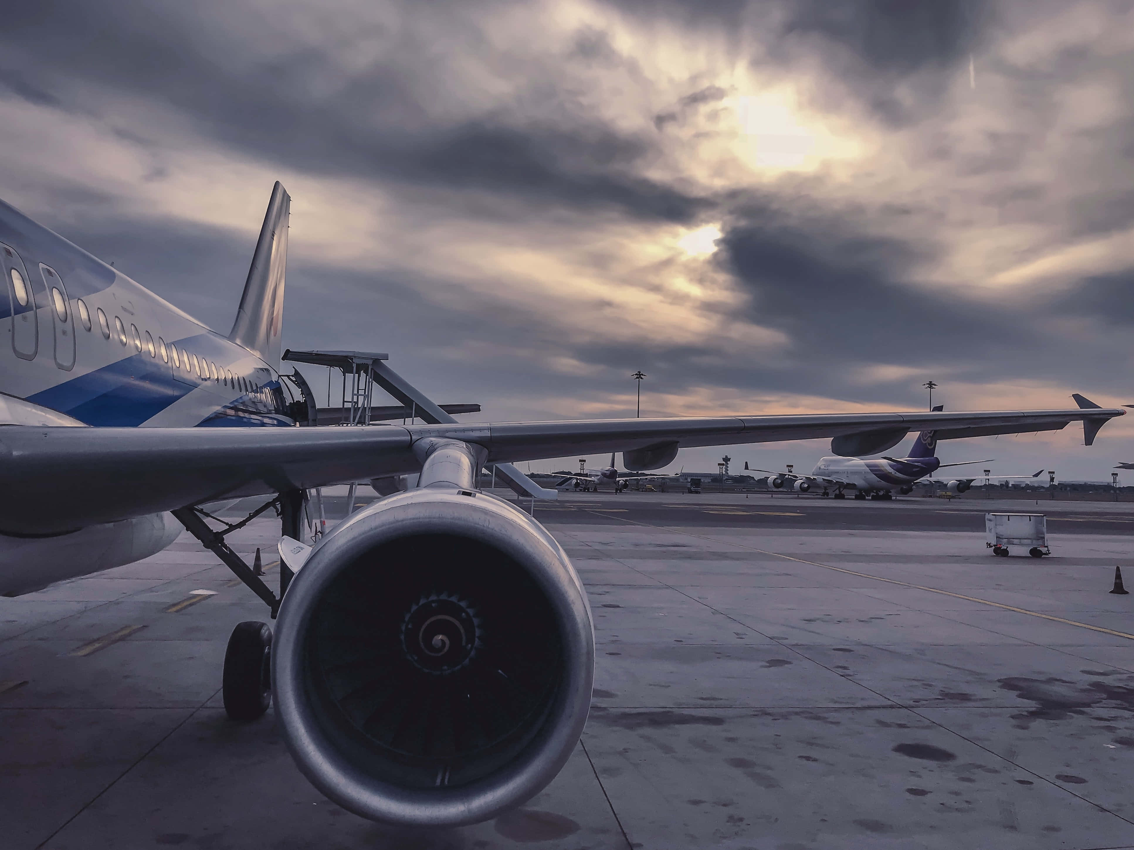 Airport 桌布 壁紙 — 一架飛機在黃昏時停泊在潮濕停機坪上，背景是戲劇性的多雲天空，近距離拍攝其噴射引擎。