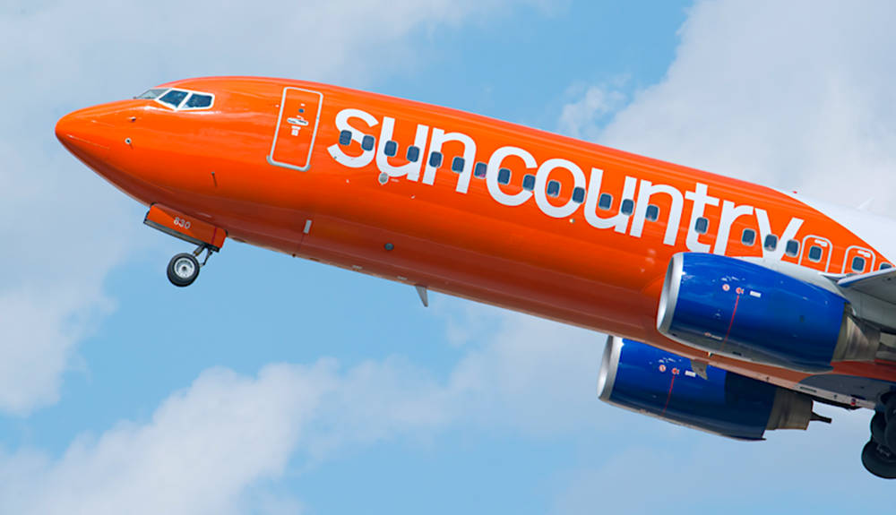 飛機 桌布 壁紙 — 一架鮮橙色、帶藍色引擎的Sun Country Airlines飛機，在點綴著蓬鬆白雲的明亮藍天中翱翔。