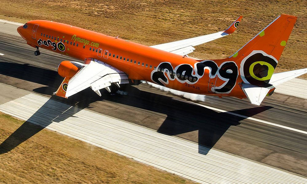 飛機 桌布 壁紙 — 一架鮮橙色的Mango Airlines飛機從跑道起飛，在停機坪上投下長長的陰影。