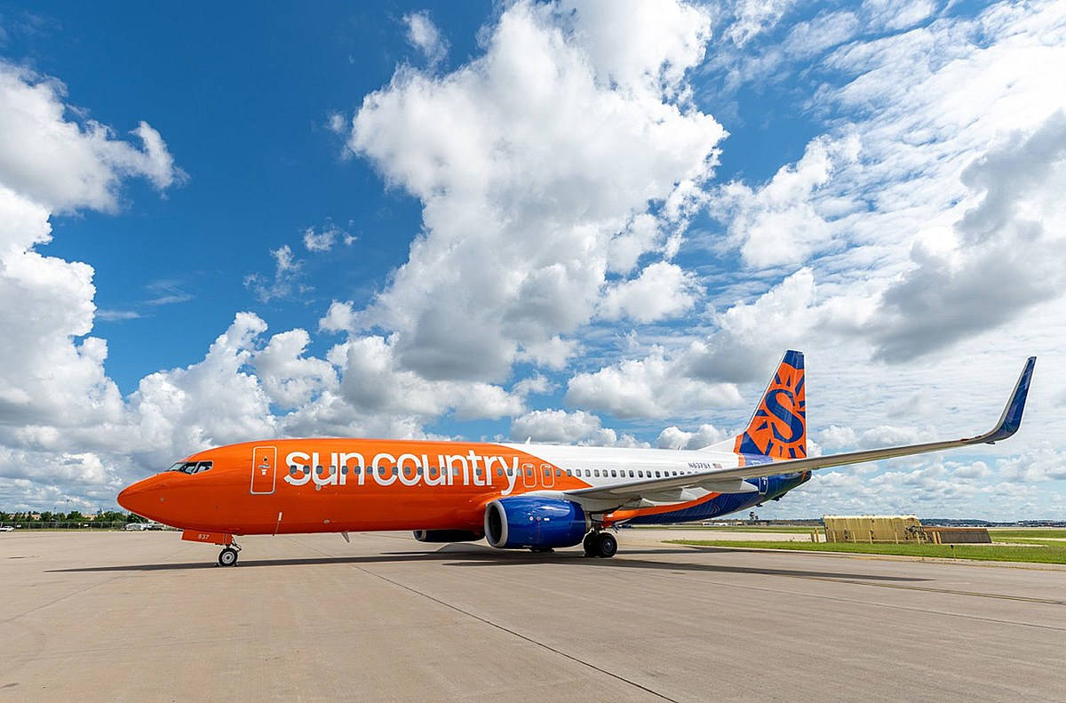 飛機 桌布 壁紙 — 一架鮮橙色的Sun Country Airlines飛機停在停機坪上，下方是充滿蓬鬆白雲的明亮藍天。