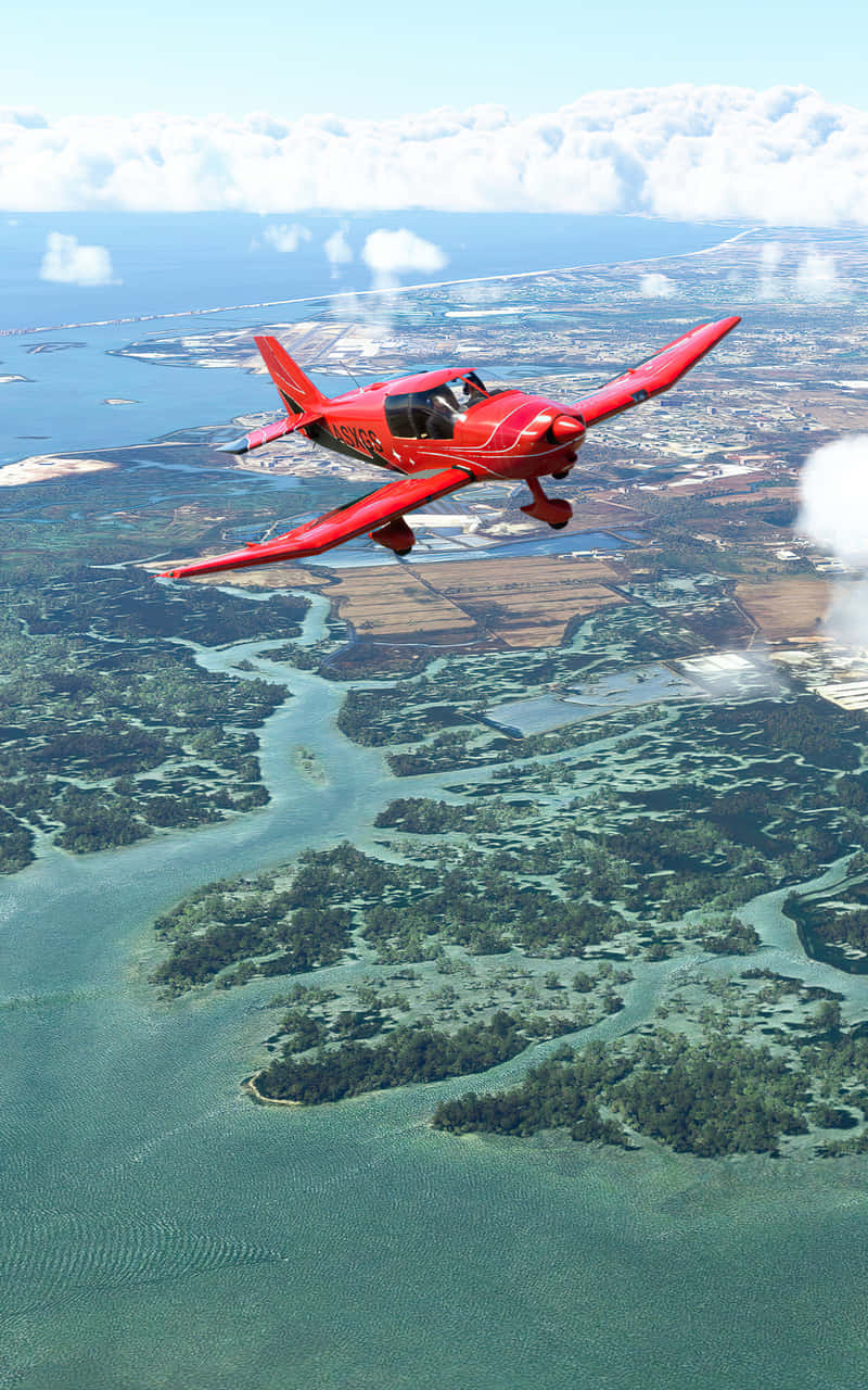 Android Microsoft Flight Simulator 桌布 壁紙 — 一架鮮紅色單引擎飛機在晴朗藍天下，翱翔於綠意盎然、水道蜿蜒的群島之上，遠方可見城市海岸線。