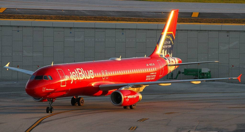 Plane 桌布 壁紙 — 一架鮮紅色的JetBlue空中巴士A320在黃金時段於機場停機坪滑行，溫暖的陽光突顯其拋光的機身。