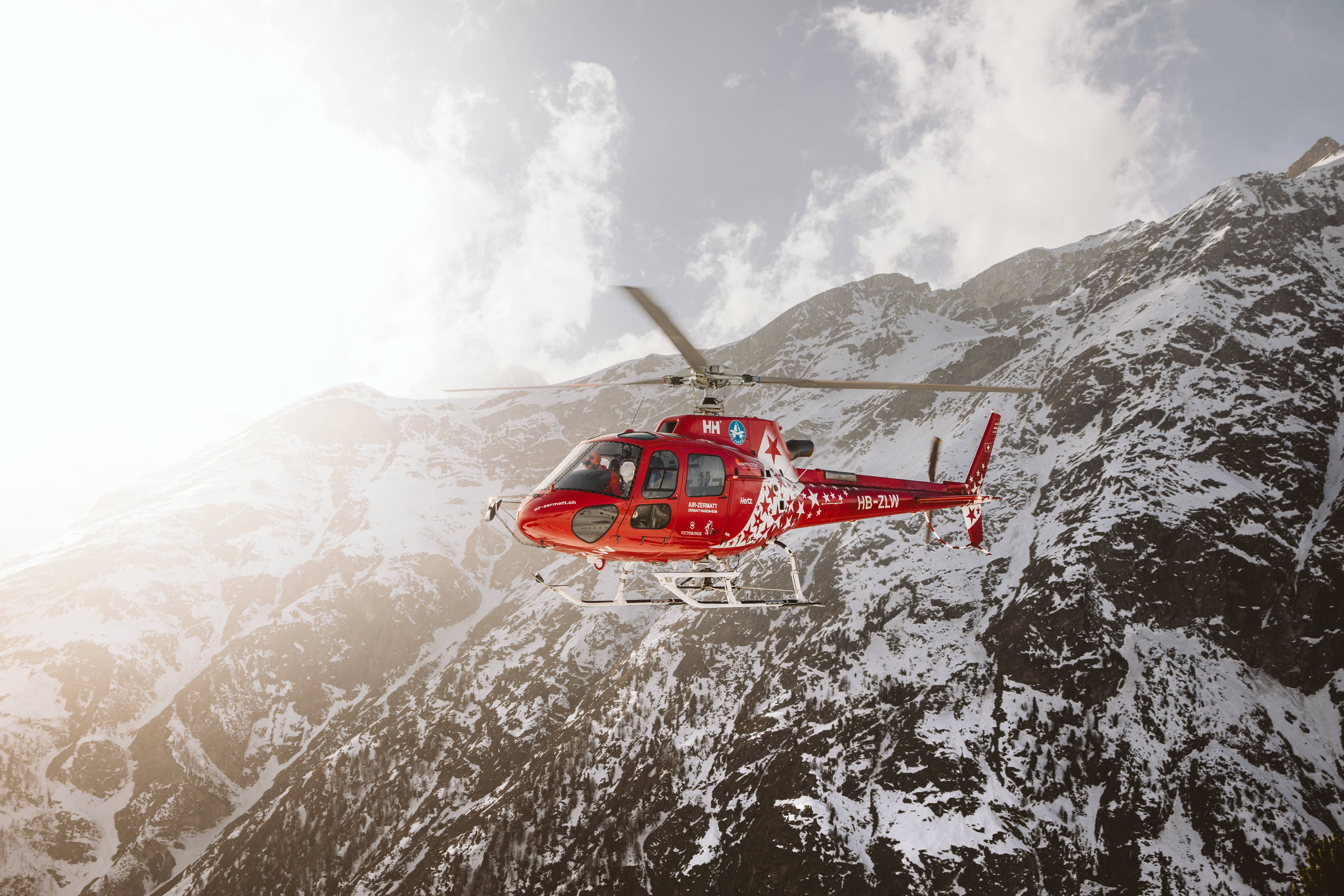 Helicopter 桌布 壁紙 — 一架鮮紅色的直升機在明亮的天空下，以積雪的山峰為背景翱翔。