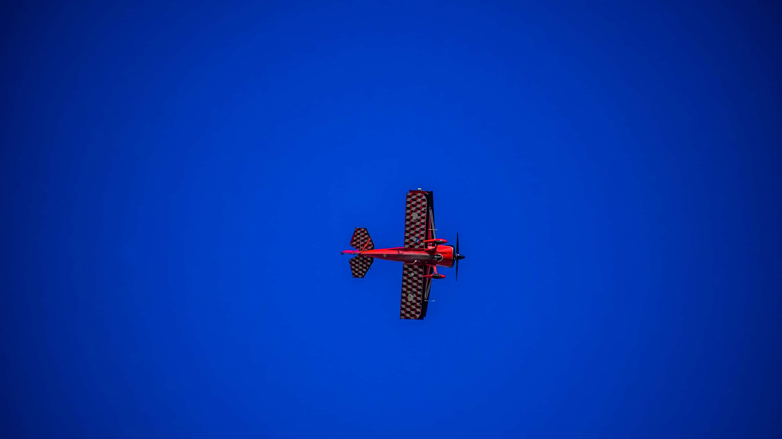 1440p Plane 桌布 壁紙 — 一架鮮紅色的雙翼飛機，帶著格子圖案的機翼，獨自翱翔在深藍色的天空。