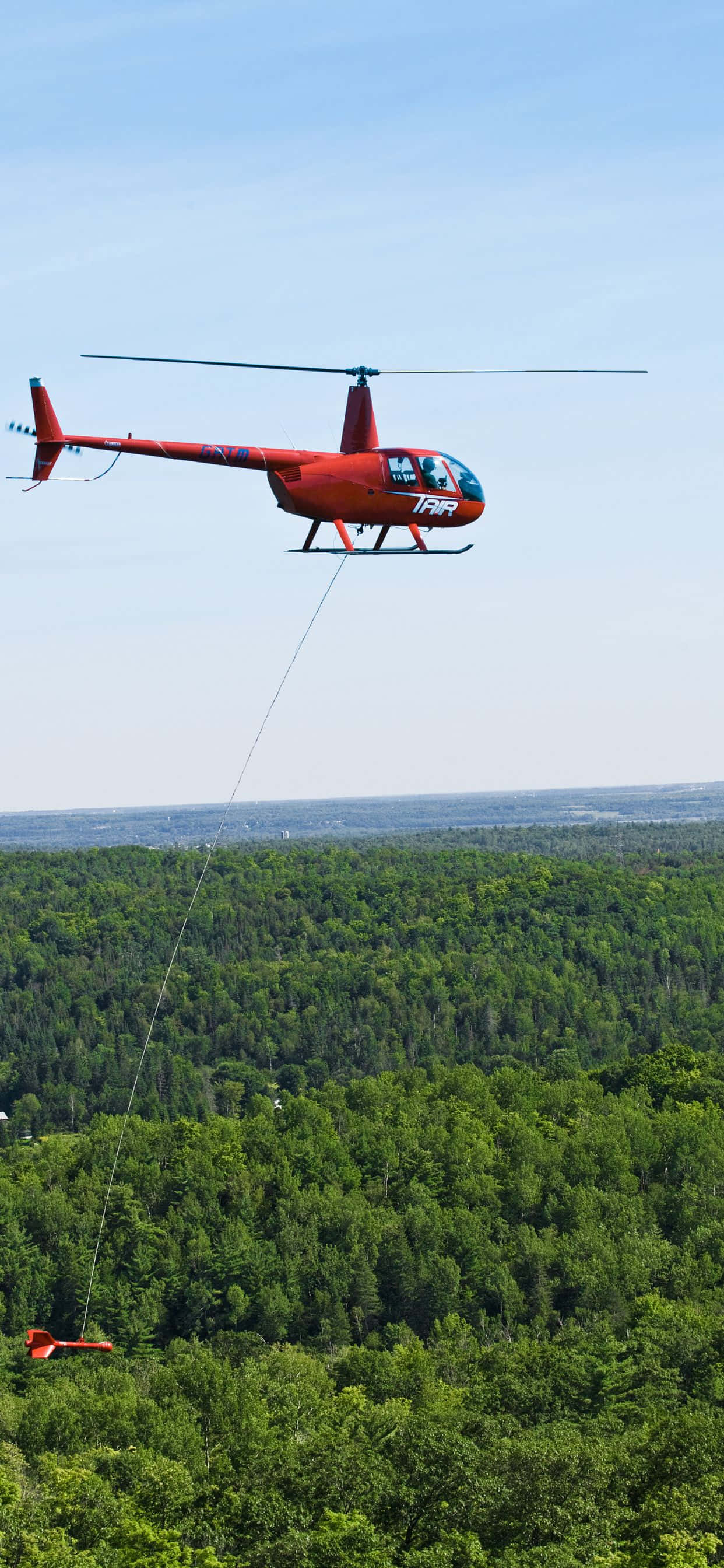 iPhone Xs Max Helicopters 桌布 壁紙 — 一架鮮紅色直升機飛過茂密的綠色森林，拖著一個紅色降落傘。