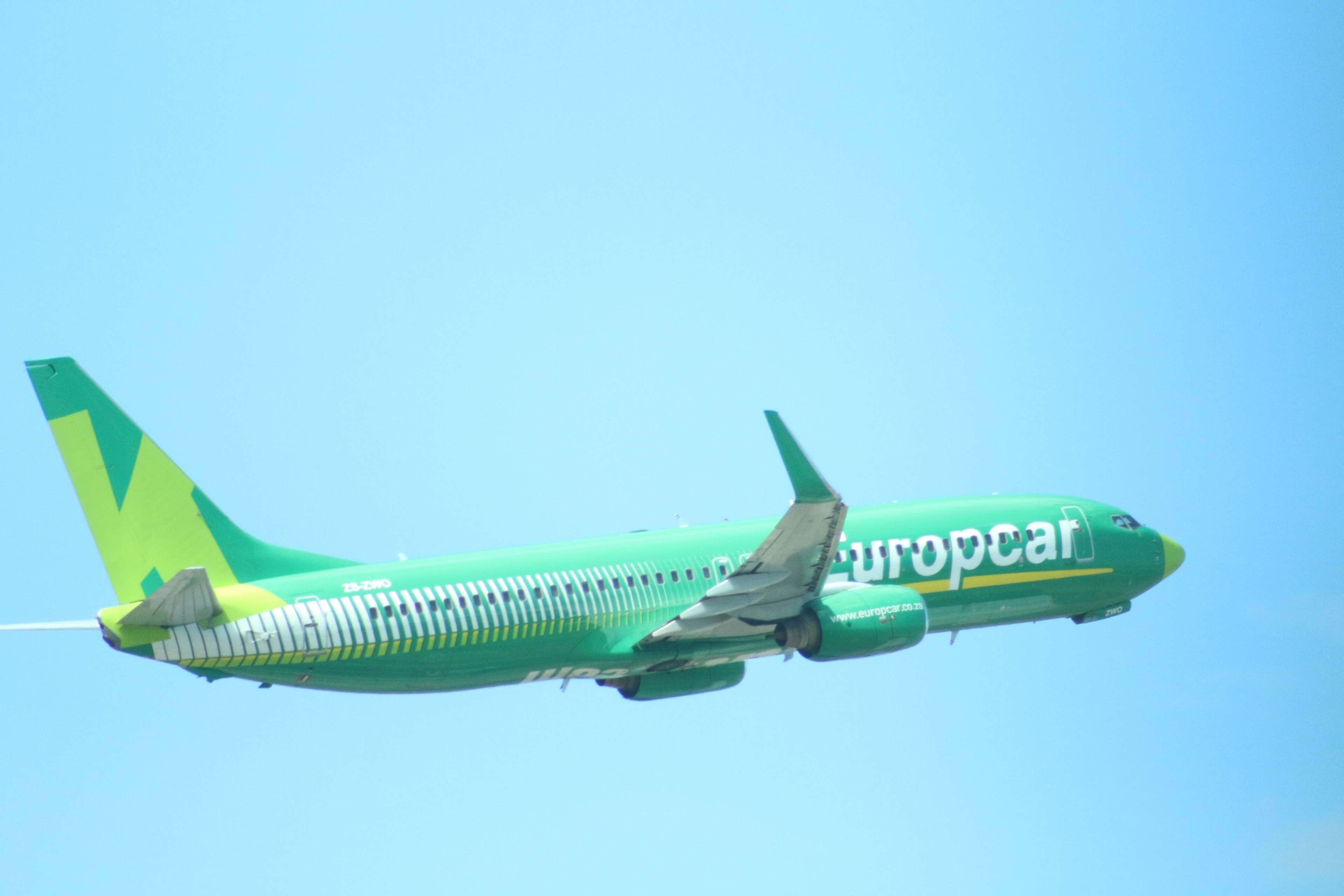 4K 飛機壁紙 桌布 壁紙 — 一架鮮綠色、帶有 Europcar 標誌的飛機，在晴朗的藍天中翱翔，雙翼展開。