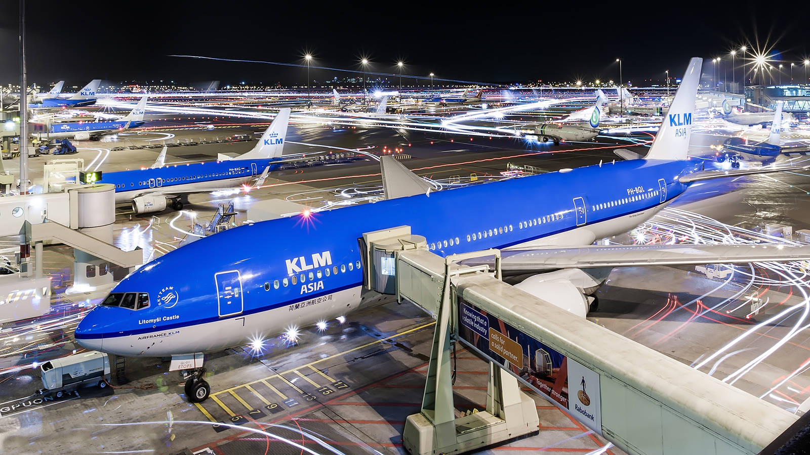 Airport 桌布 壁紙 — 一架鮮藍色的KLM亞洲飛機在夜間停泊在機場閘口，移動車輛的光軌照亮停機坪。