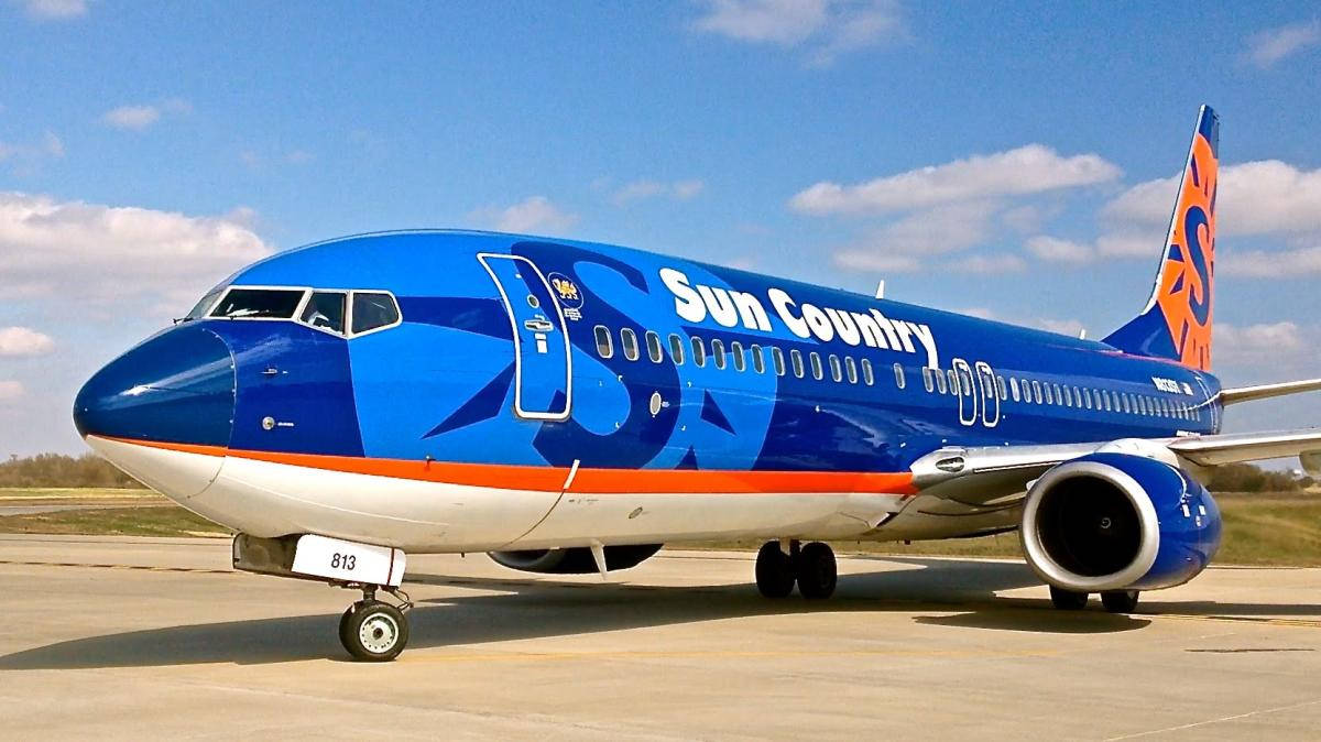 Airport 桌布 壁紙 — 一架鮮藍色的Sun Country Airlines飛機，帶有橙色點綴，停在陽光普照的停機坪上，天空晴朗。