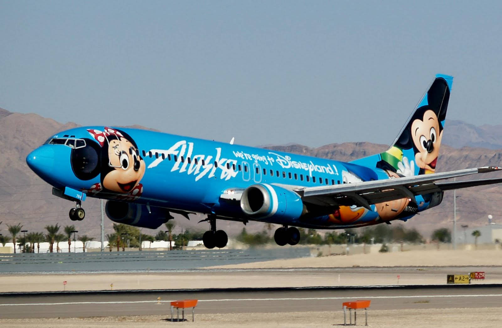 飛機 桌布 壁紙 — 一架鮮藍色阿拉斯加航空飛機，帶有米奇和米妮老鼠塗裝，在沙漠背景下起飛。