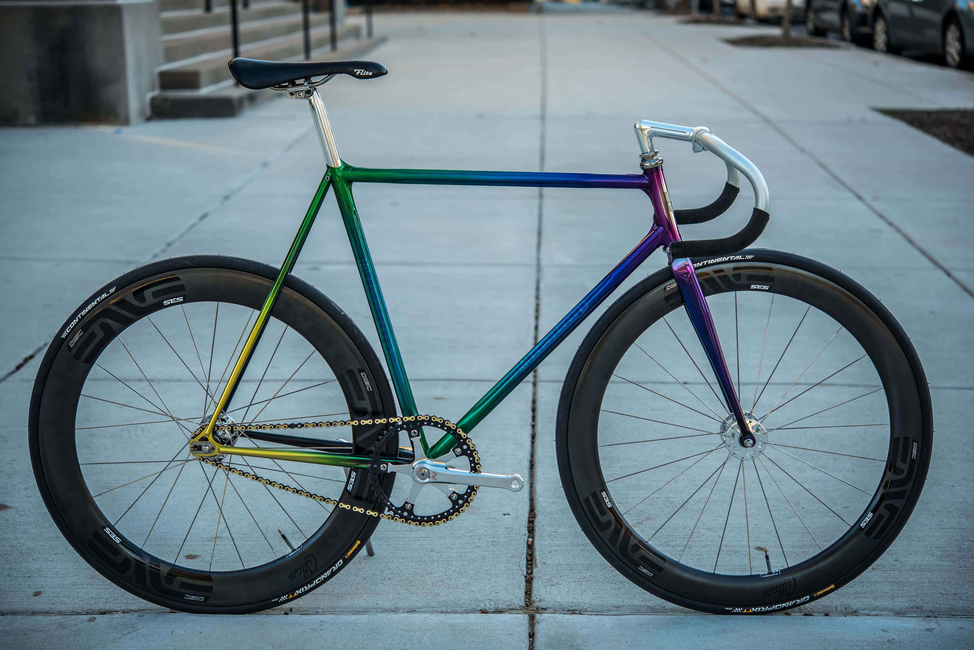 Bicycle 桌布 壁紙 — 一架鮮豔的彩虹色固定齒輪腳踏車佇立在混凝土人行道上，其流線型車架在柔和日光下閃閃發光。