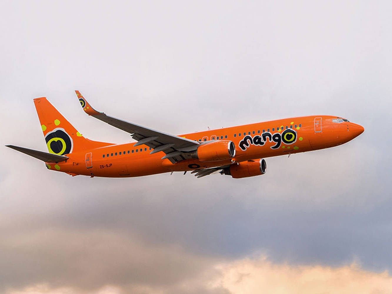 雲朵 桌布 壁紙 — 一架鮮豔的橙色Mango Airlines飛機在多雲的天空中翱翔，下方夕陽色調閃耀。