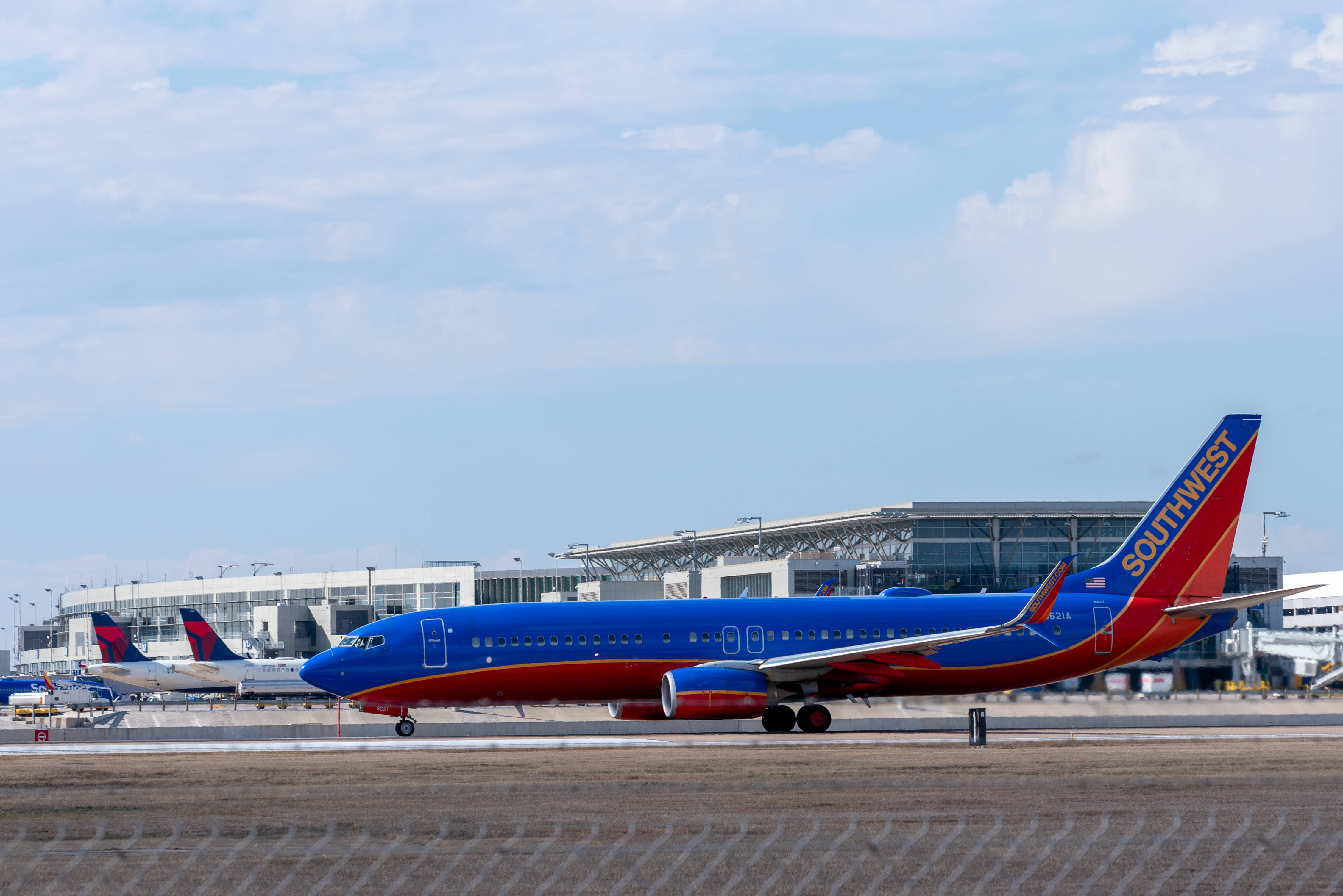 Aerospace 桌布 壁紙 — 一架鮮豔的藍紅相間西南航空噴射機在陽光明媚的機場停機坪上滑行，背景是航站樓建築。