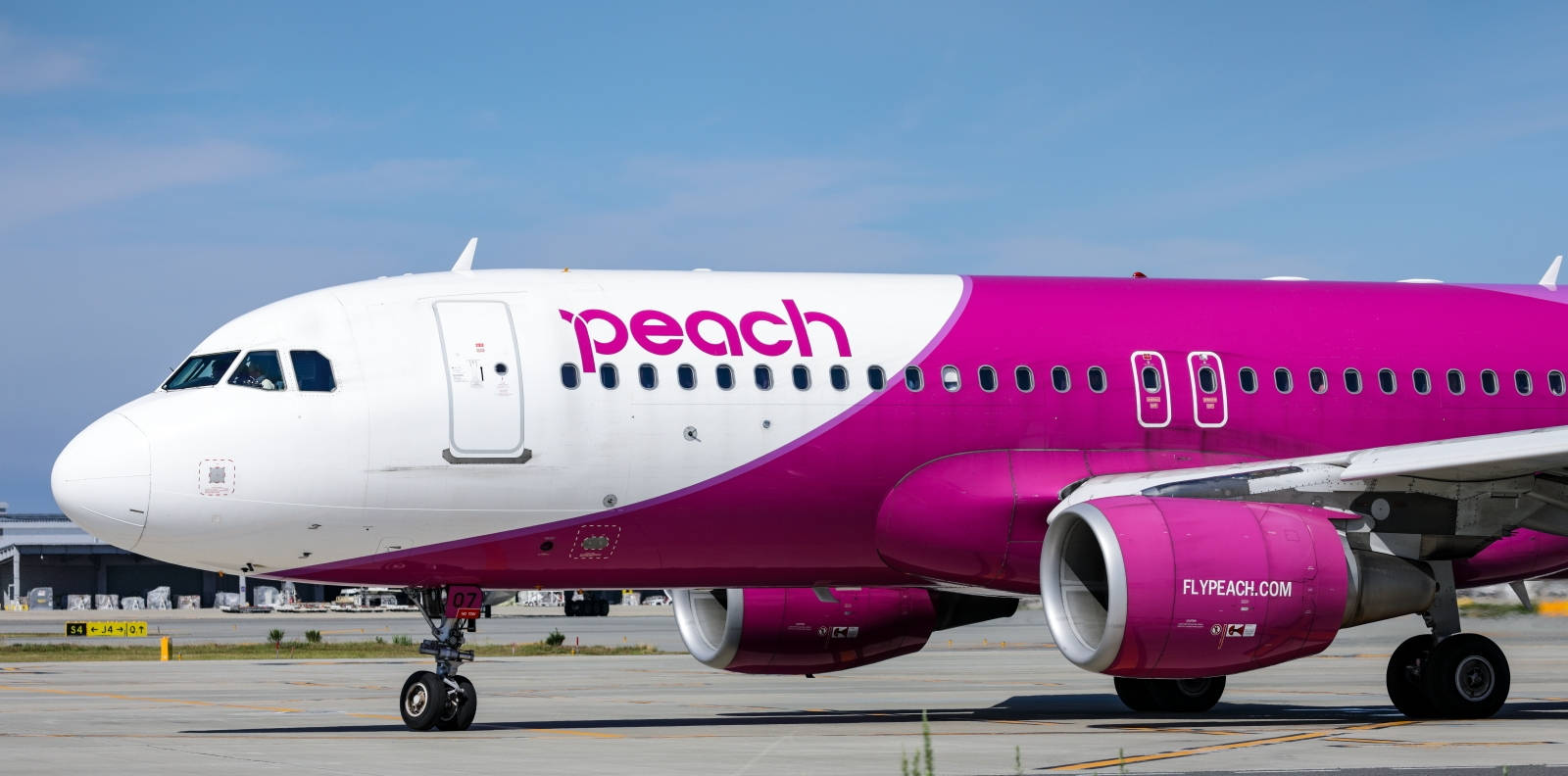 Airport 桌布 壁紙 — 一架鮮豔粉紅和白色的Peach Airlines飛機停在陽光明媚的機場停機坪上，天空清澈湛藍。