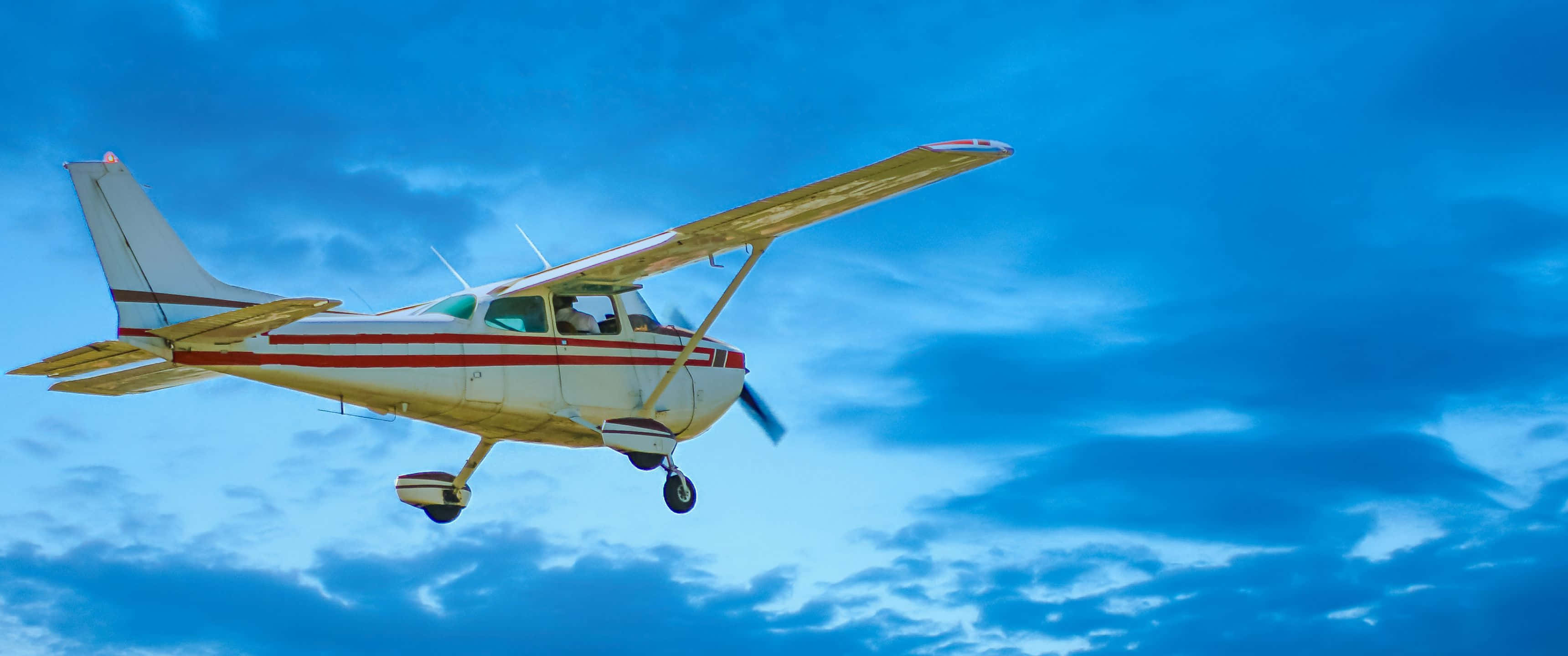 3440x1440p Small Planes 桌布 壁紙 — 一架黃白相間的單引擎飛機在藍天白雲中翱翔。