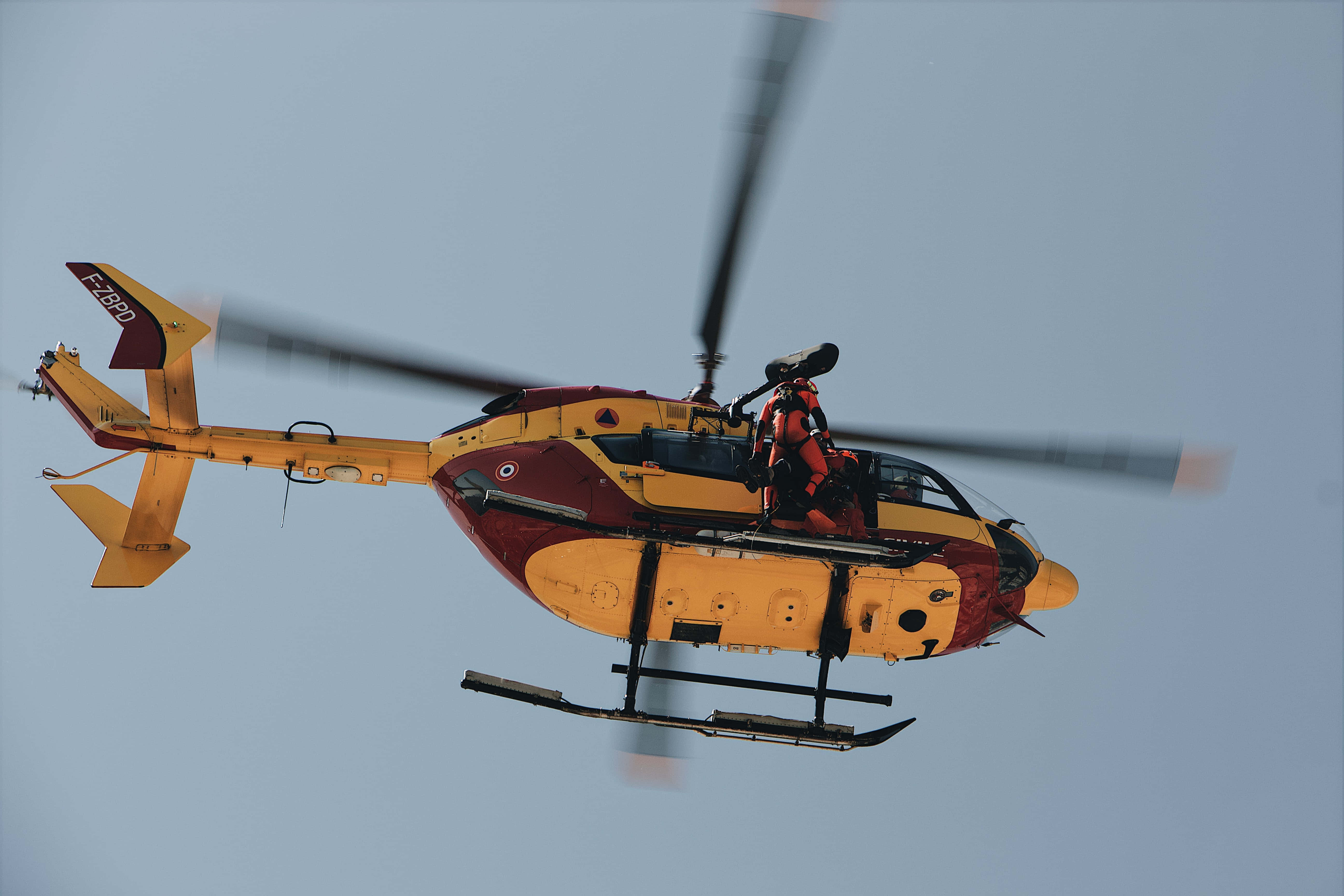 Helicopter 桌布 壁紙 — 一架黃色和栗紅色的救援直升機旋轉著葉片，在清澈的淡藍色天空中翱翔。