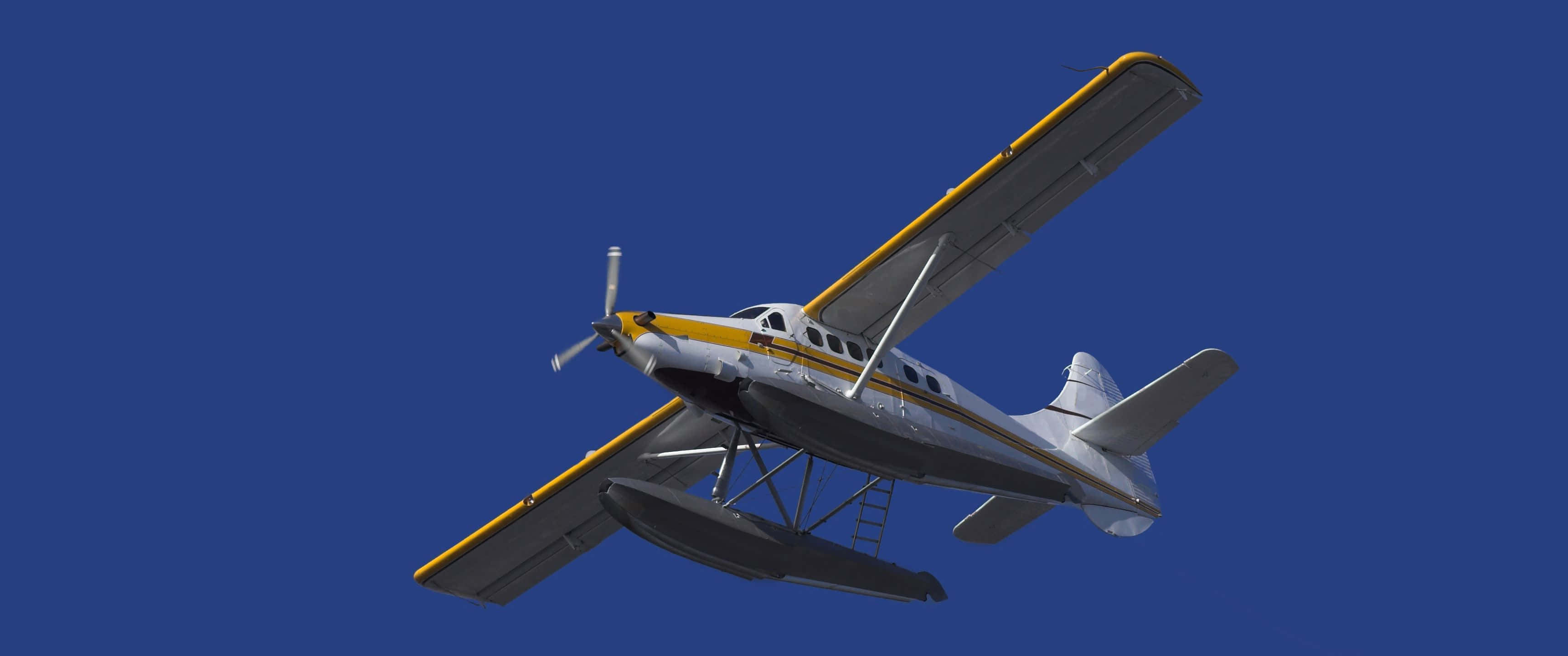 3440x1440p Small Planes 桌布 壁紙 — 一架黃色和銀色的水上飛機在無雲的清澈深藍天空中翱翔。