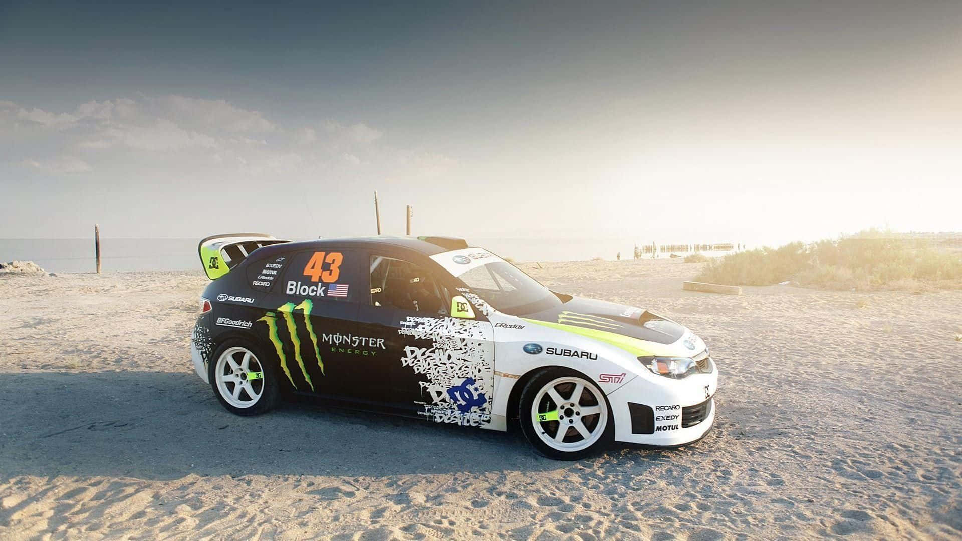 1080p Dirt 3 桌布 壁紙 — 一架黑白配色的Subaru拉力賽車，帶有Monster Energy塗裝，停泊在陽光明媚的沙灘上，靠近海洋。