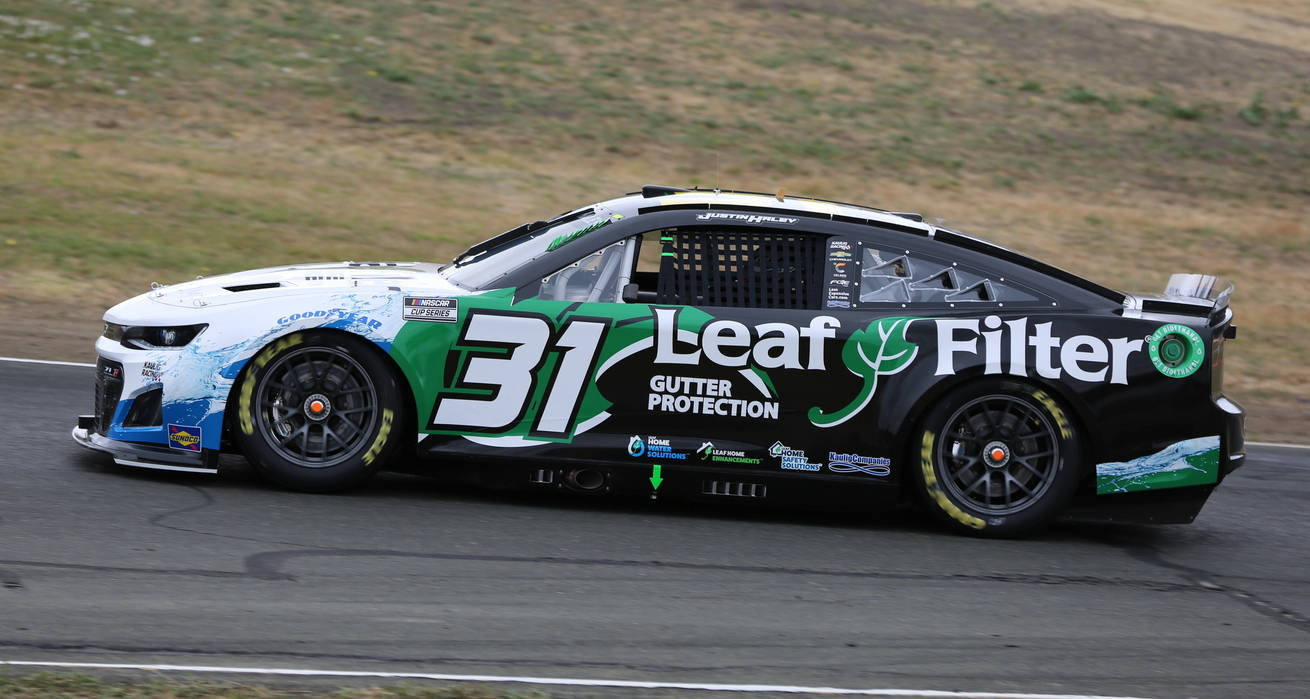 Road 桌布 壁紙 — 一架黑色、綠色和白色的 #31 Leaf Filter NASCAR 賽車在賽道上疾馳，背景是模糊的草地山丘。