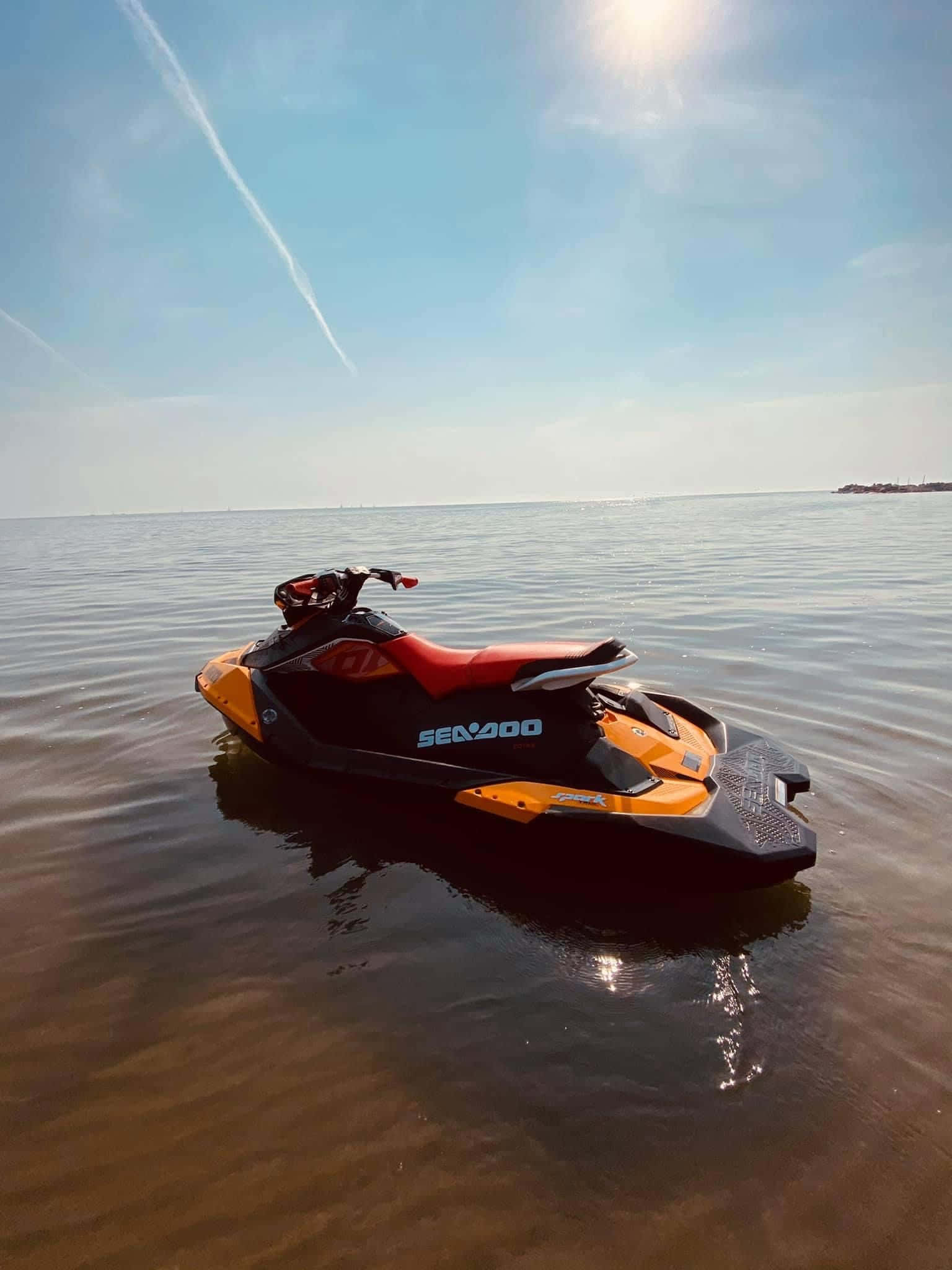 太陽 桌布 壁紙 — 一架黑色和橙色的 Sea-Doo 水上摩托車在平靜的棕色水面上漂浮，天空湛藍，有凝結尾跡。