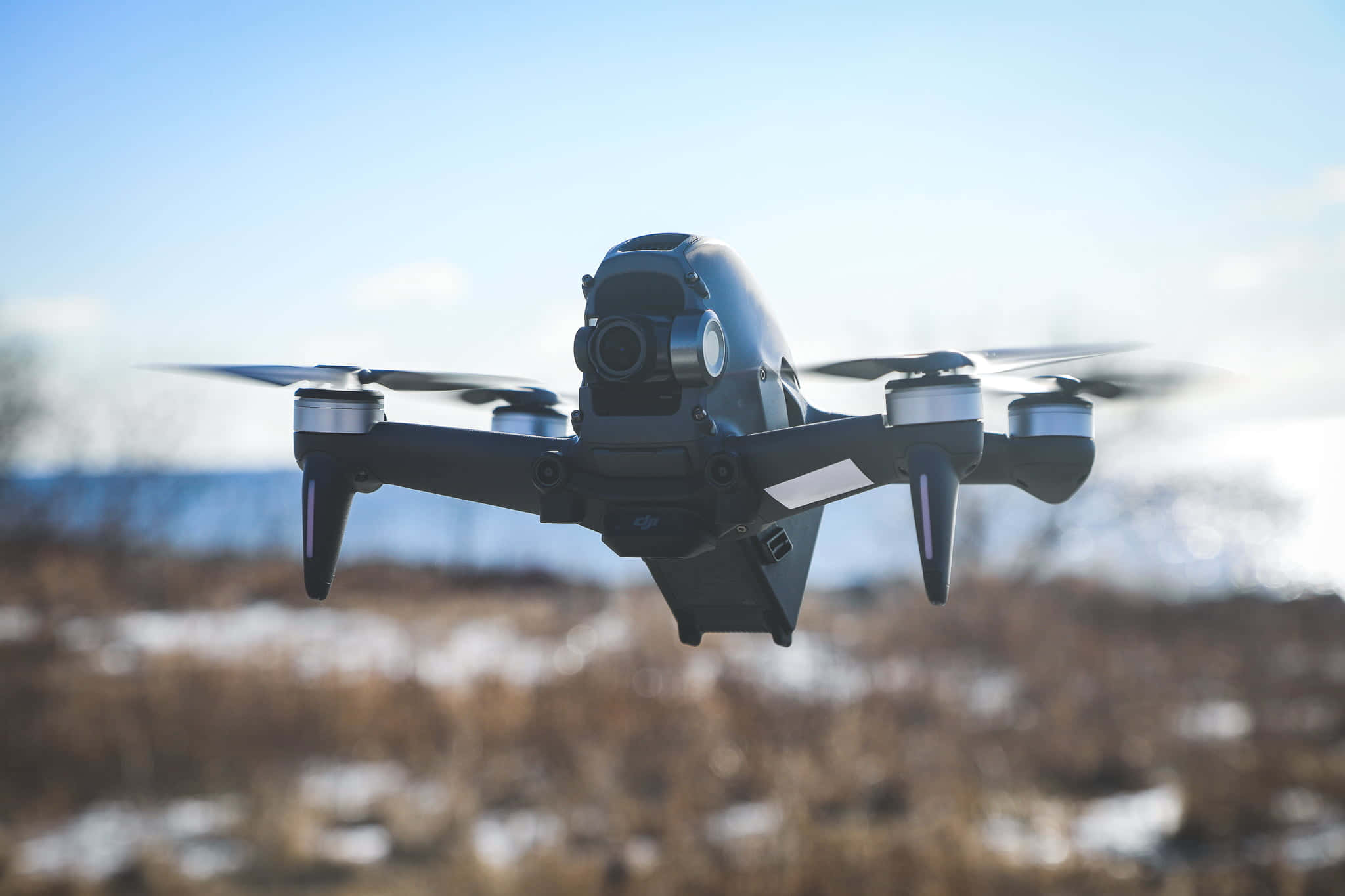 drone 桌布 壁紙 — 一架黑色無人機在清澈的藍天中懸停，下方是模糊的雪地。
