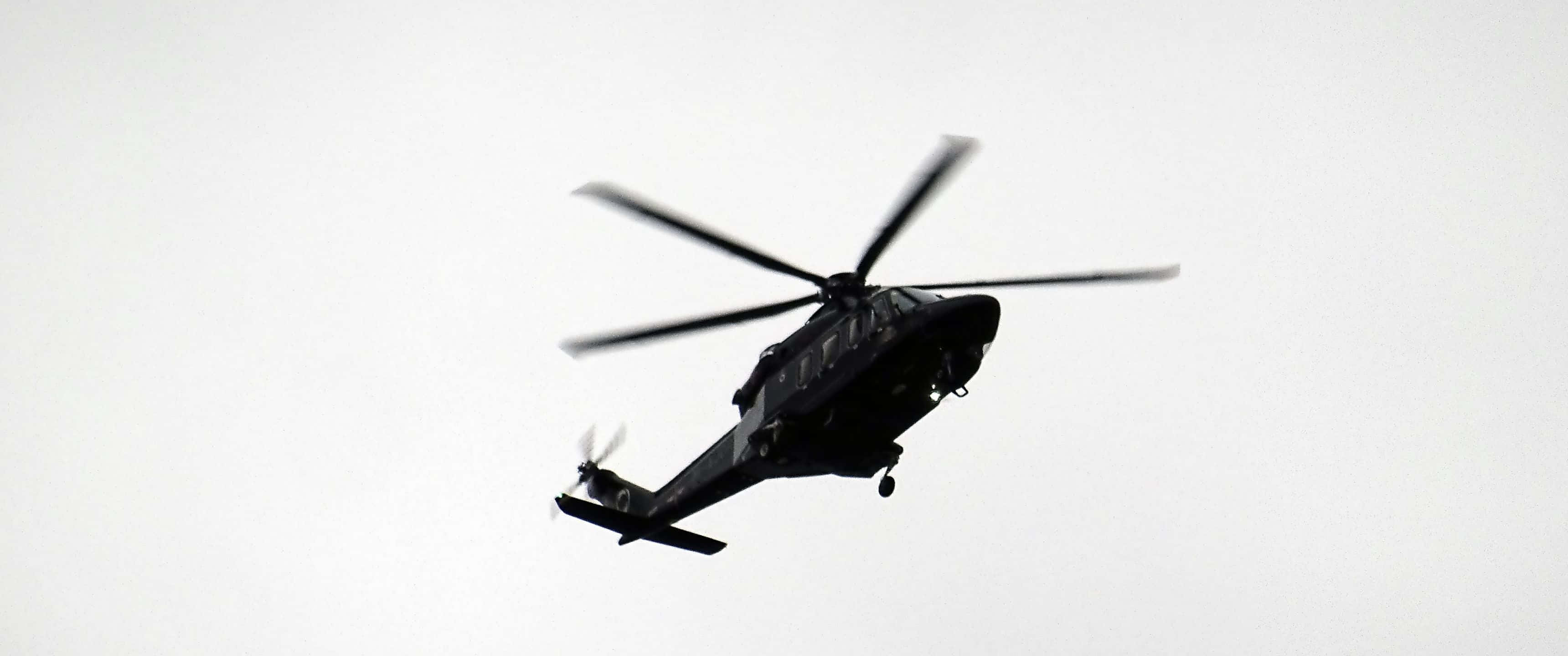 3440x1440p Helicopters 桌布 壁紙 — 一架黑色直升機在明亮多雲的天空中呈現剪影，旋翼轉動。