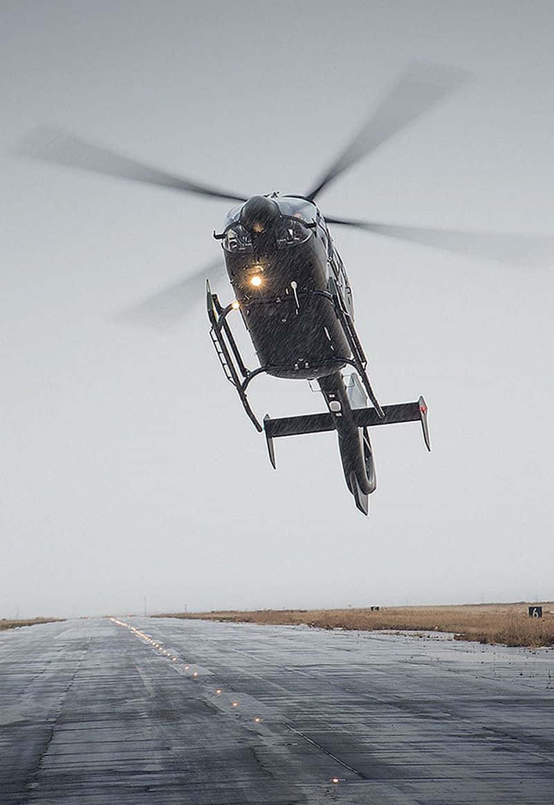 Helicopters 桌布 壁紙 — 一架黑色直升機在灰色天空下低空盤旋於潮濕的跑道上，旋翼轉動。