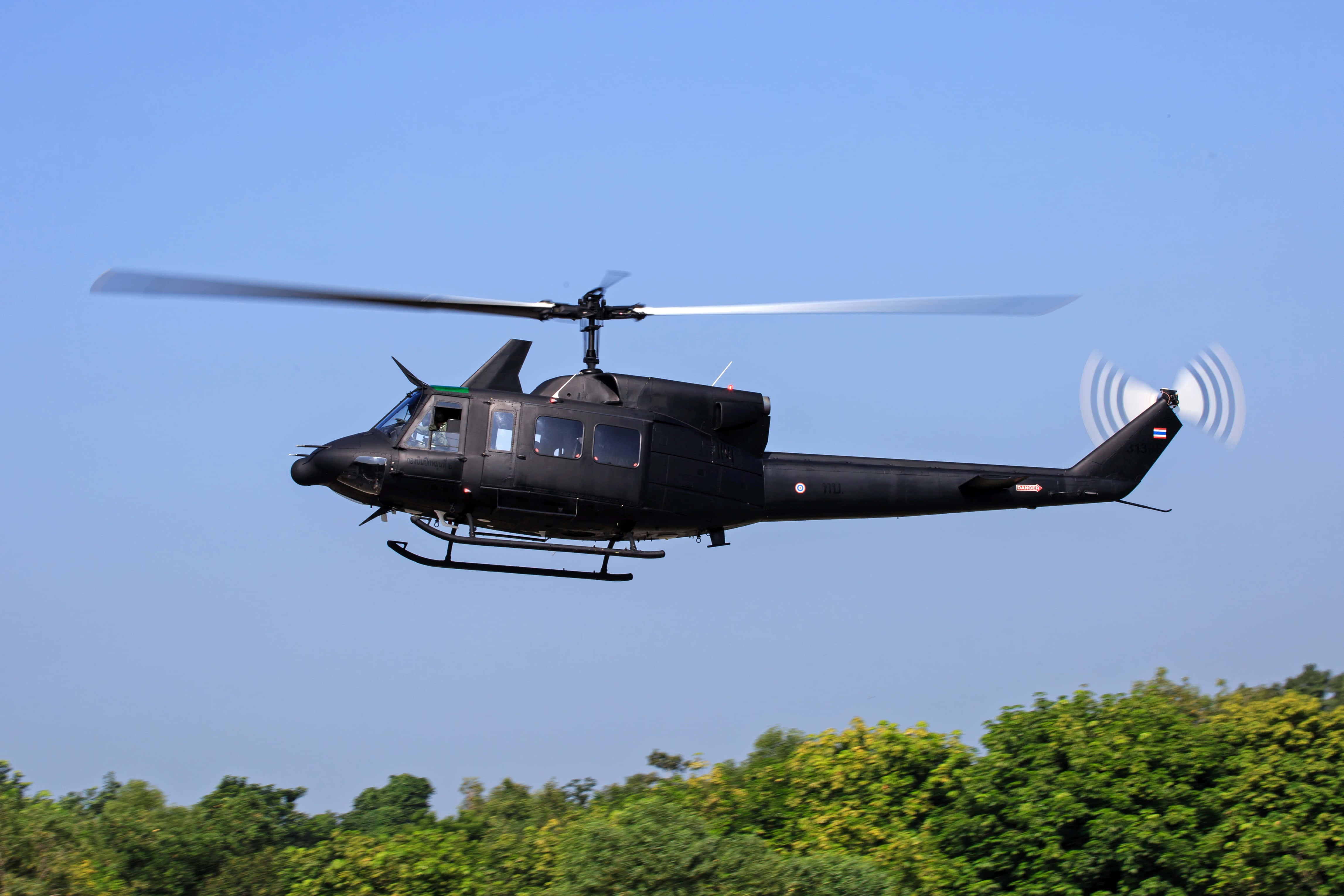 Helicopter 桌布 壁紙 — 一架黑色軍用直升機在晴朗藍天下盤旋於茂密綠樹之上。