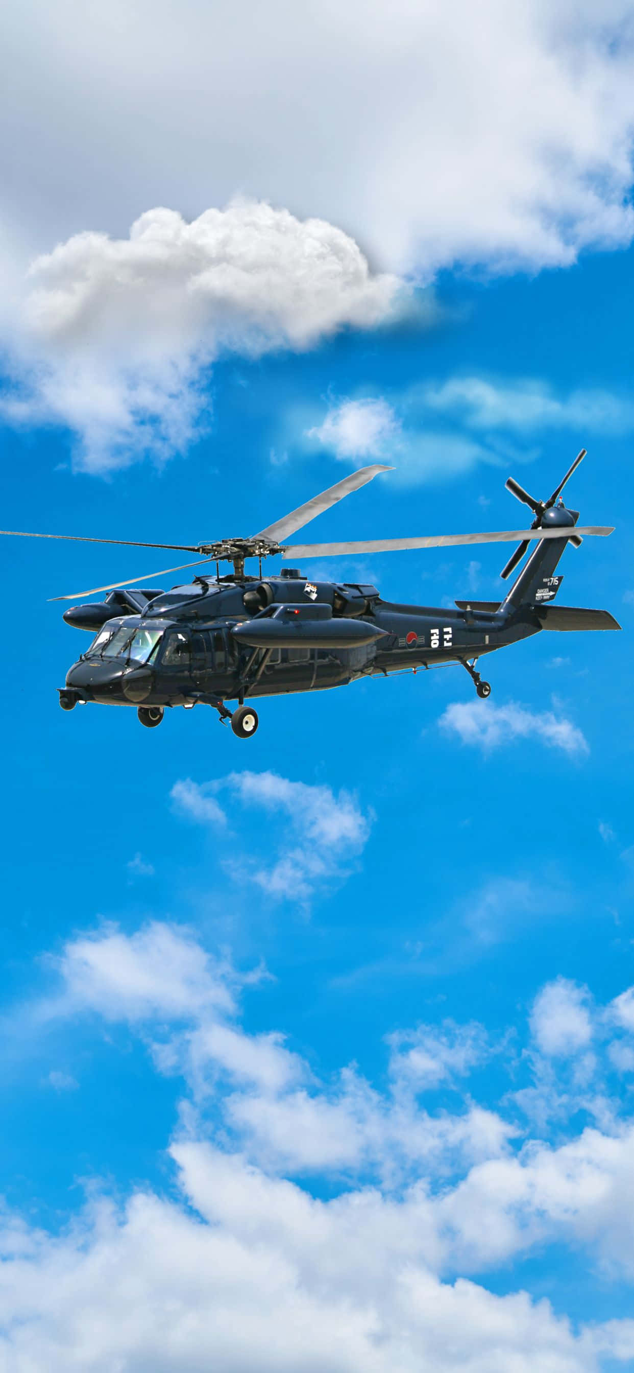 iPhone Xs Max Helicopters 桌布 壁紙 — 一架黑色軍用直升機在點綴著蓬鬆白雲的明亮藍天中翱翔。