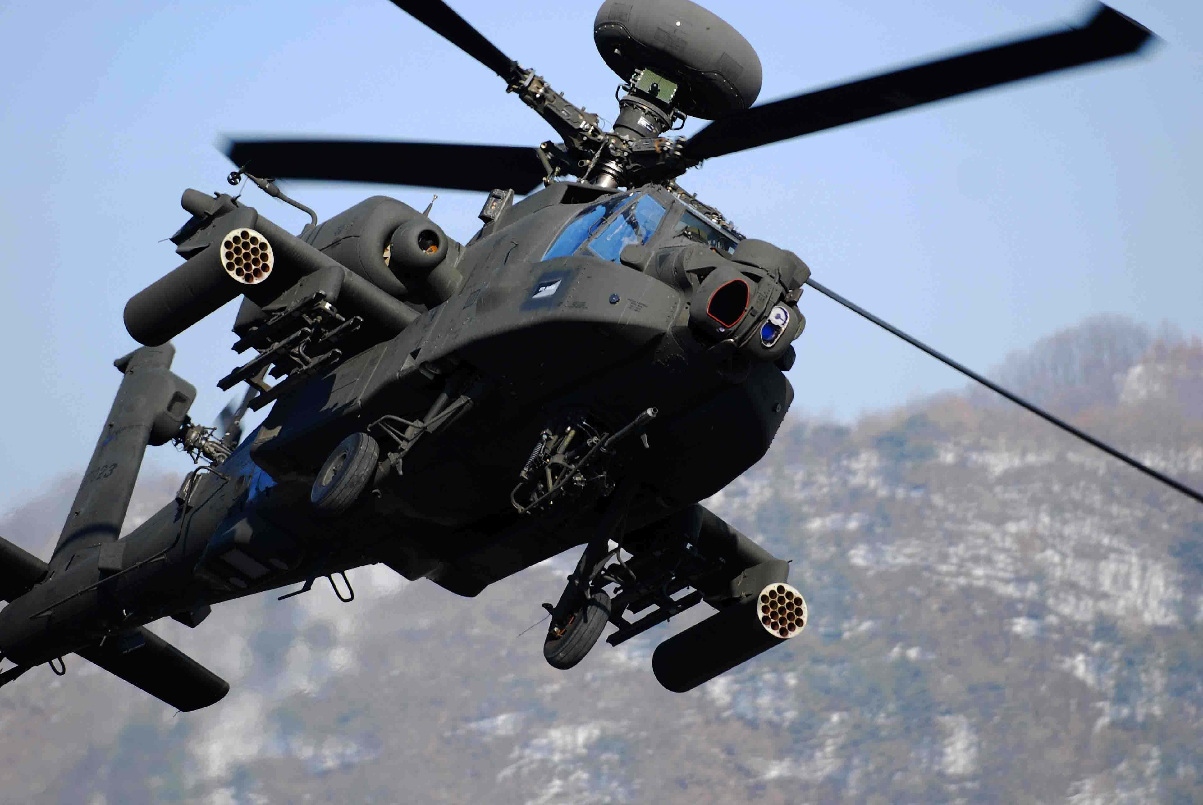 4K Helicopters 桌布 壁紙 — 一架黑色軍用直升機配備武器，在藍天白雲下，以積雪的山脈為背景盤旋。