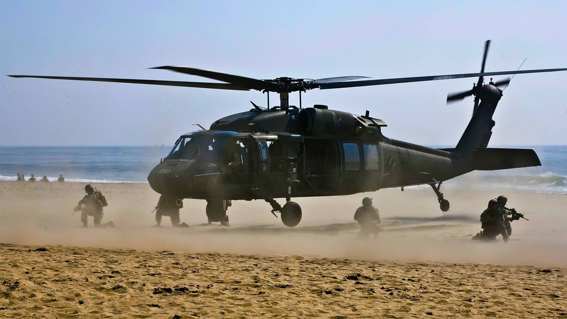 Helicopter 桌布 壁紙 — 一架黑色軍用直升機降落在沙灘上，士兵們在海洋附近圍繞它移動。