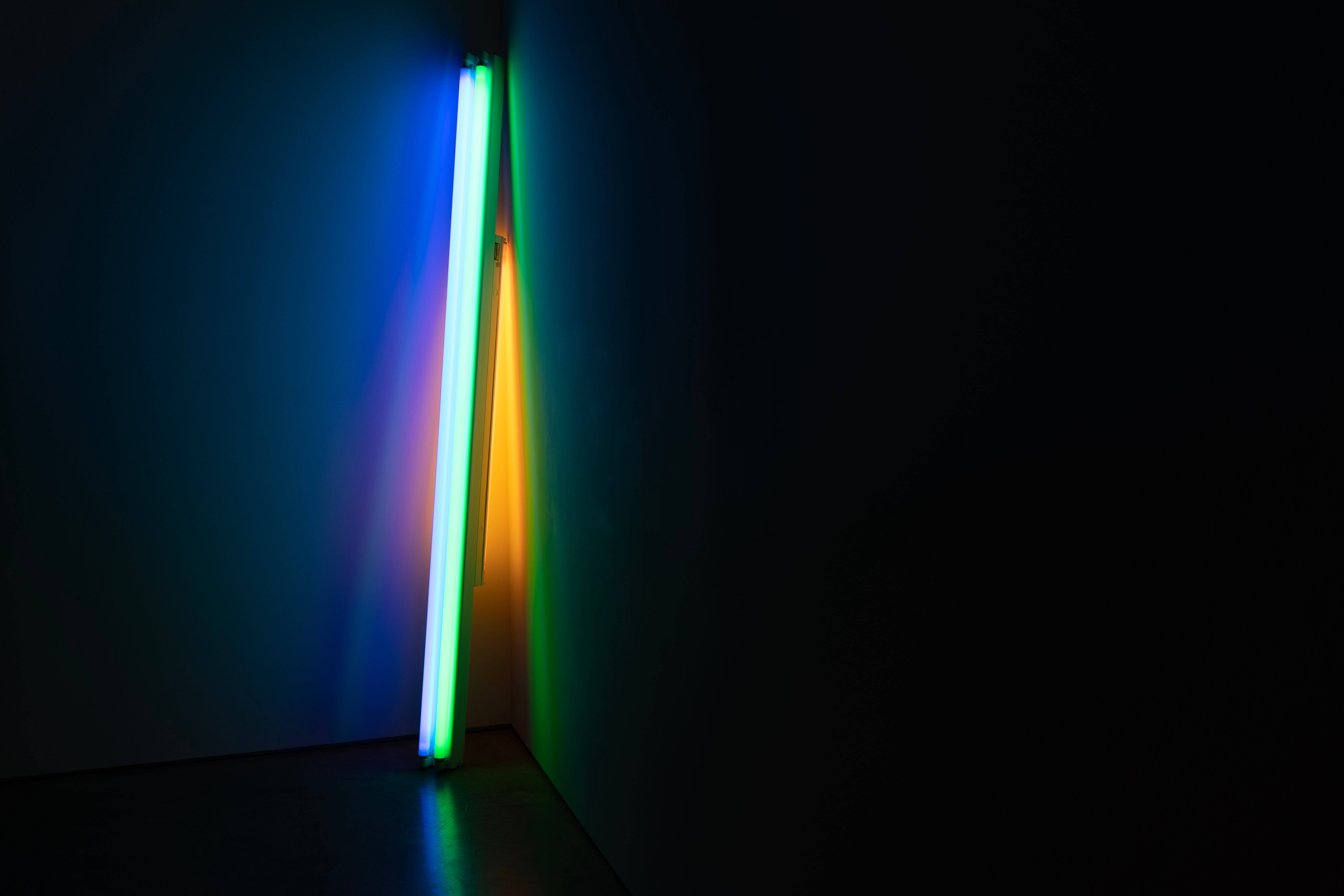 Dark Neon 桌布 壁紙 — 一根充滿活力的霓虹燈管，散發著藍色、綠色和黃色的色調，在黑暗的房間角落投射出色彩繽紛的反射。