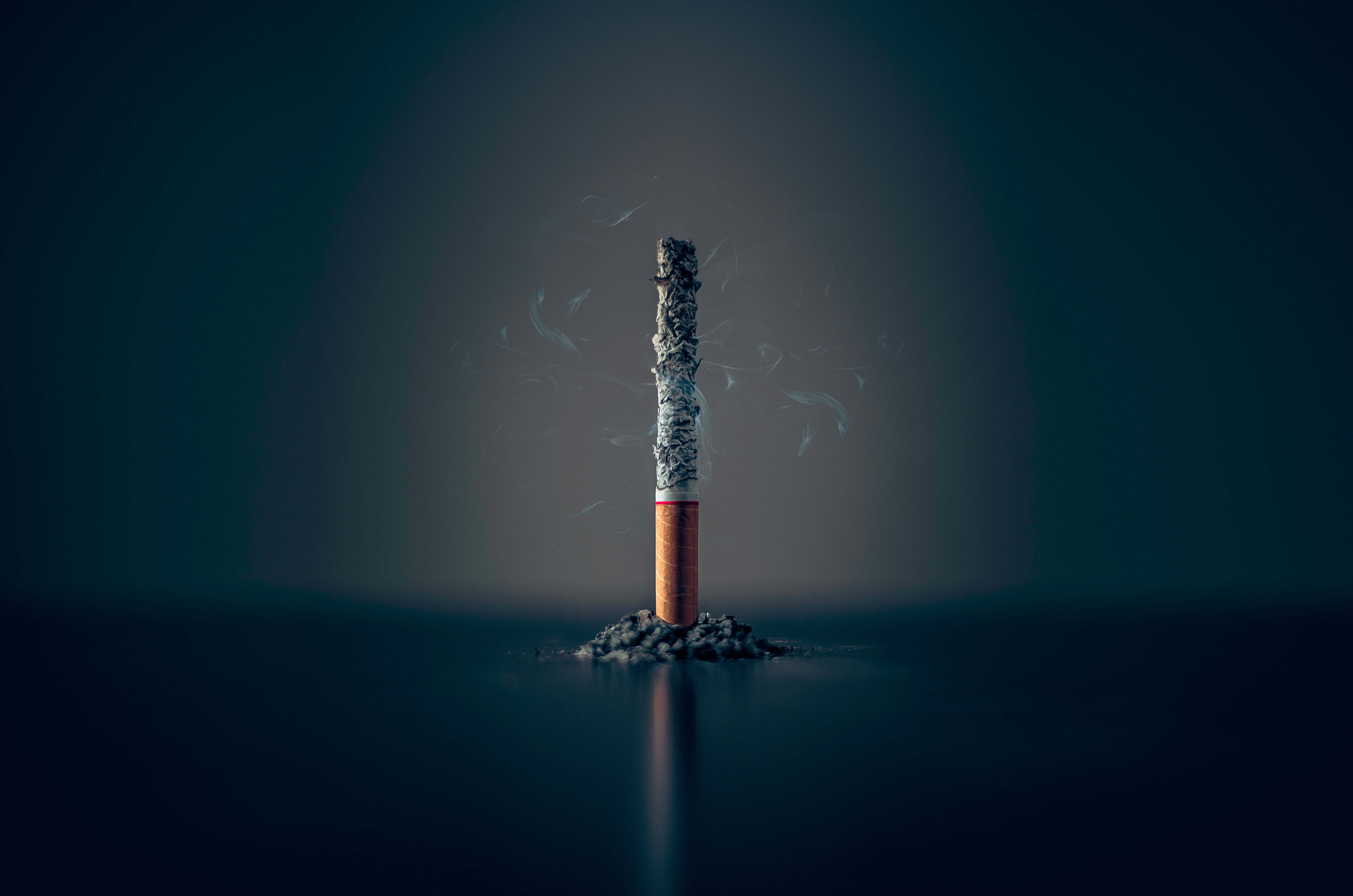 Addiction 桌布 壁紙 — 一根冒煙的香煙直立於反光暗面上的灰燼中，縷縷煙霧在漸變背景襯托下向上繚繞。