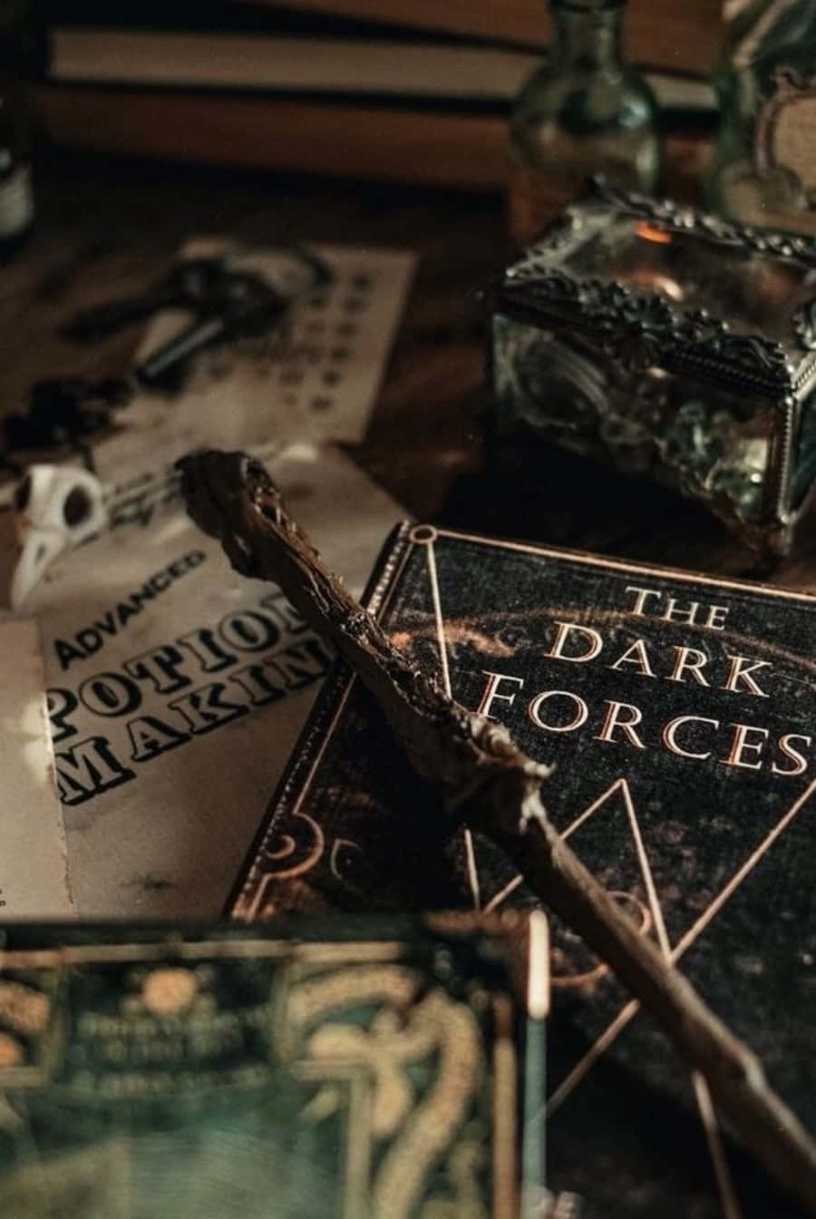 哈利波特 美學 桌布 壁紙 — 一根深色木魔杖放在一本名為《The Dark Forces》的書上，旁邊有魔藥製作筆記和華麗的玻璃瓶，在昏暗的書房中。