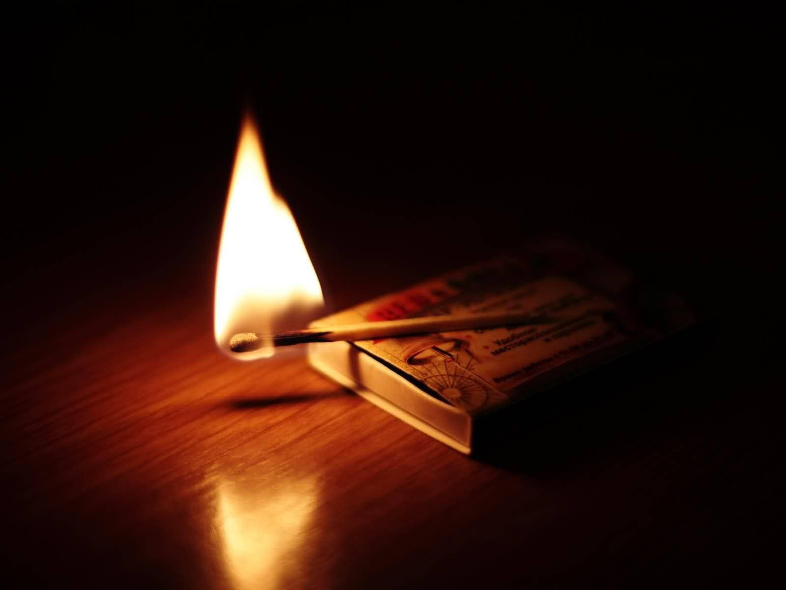 火焰動畫 桌布 壁紙 — 一根燃燒的火柴在黑暗背景下，在木質表面上投射出溫暖的金色光芒。