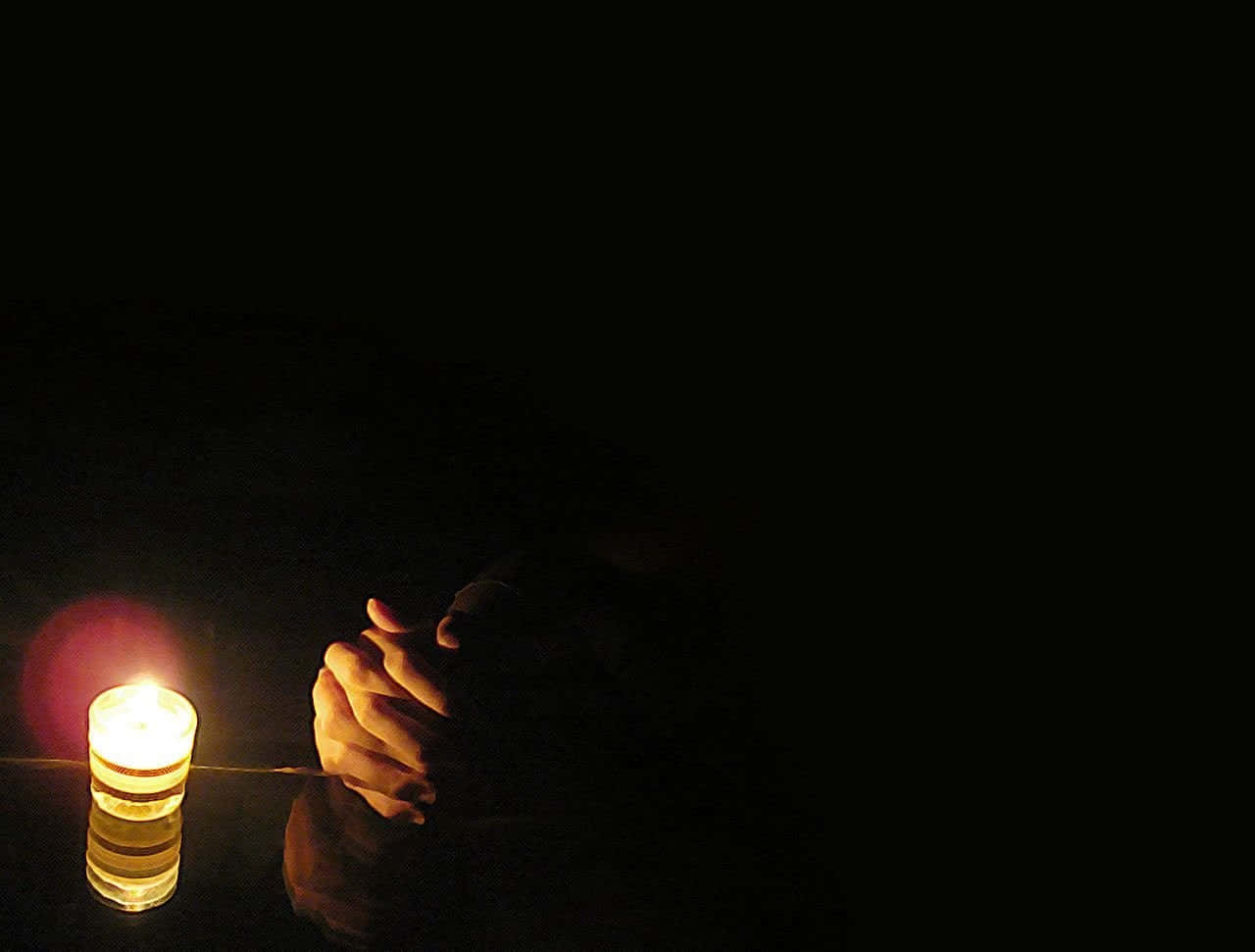 Praying 桌布 壁紙 — 一根蠟燭在黑暗的房間中將溫暖的光芒投射在緊握的雙手上，營造出安靜沉思的氛圍。