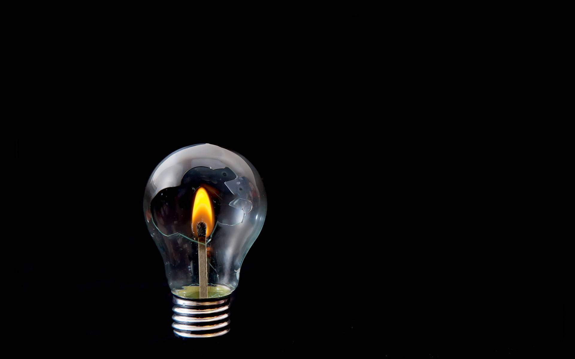 Light 桌布 壁紙 — 一根點燃的火柴在透明燈泡內，在純黑背景下散發出溫暖的光芒。