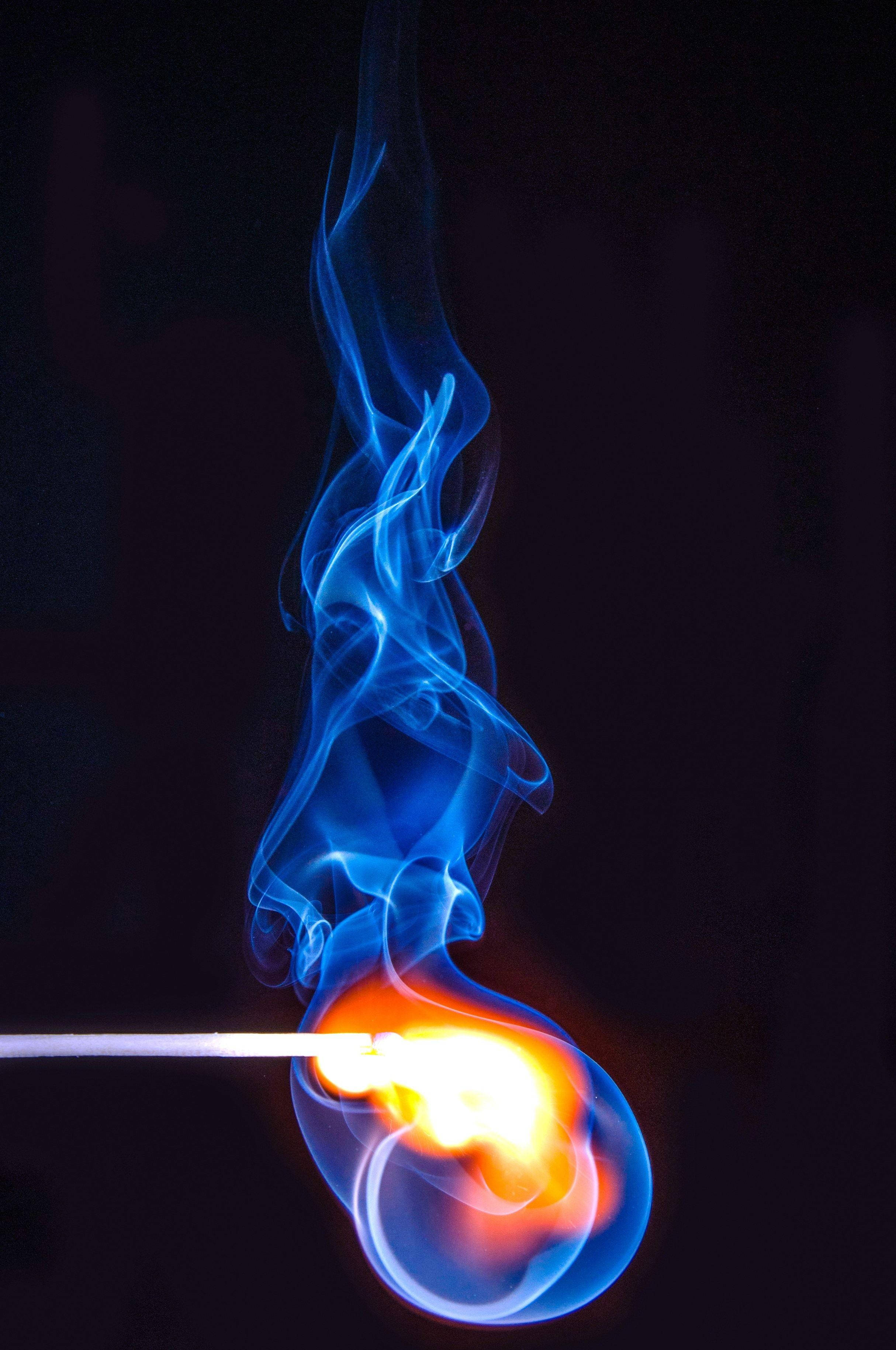 Flame 桌布 壁紙 — 一根點燃的火柴在黑暗背景下投射出鮮豔的橙色火焰和旋轉的藍色煙霧。