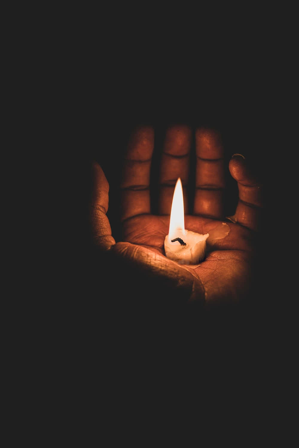 死亡 桌布 壁紙 — 一根點燃的蠟燭放在張開的手掌上，在漆黑的背景下投射出溫暖的光芒。