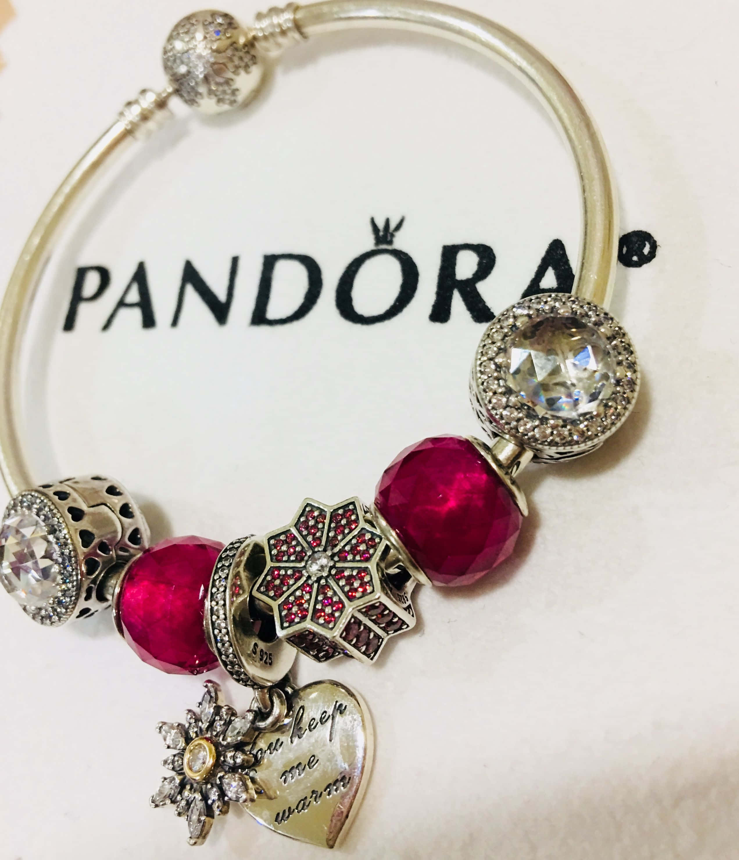 潘朵拉 桌布 壁紙 — 一條 Pandora 飾品手鍊，帶有紅色珠子和閃爍飾品，放置在品牌包裝上。