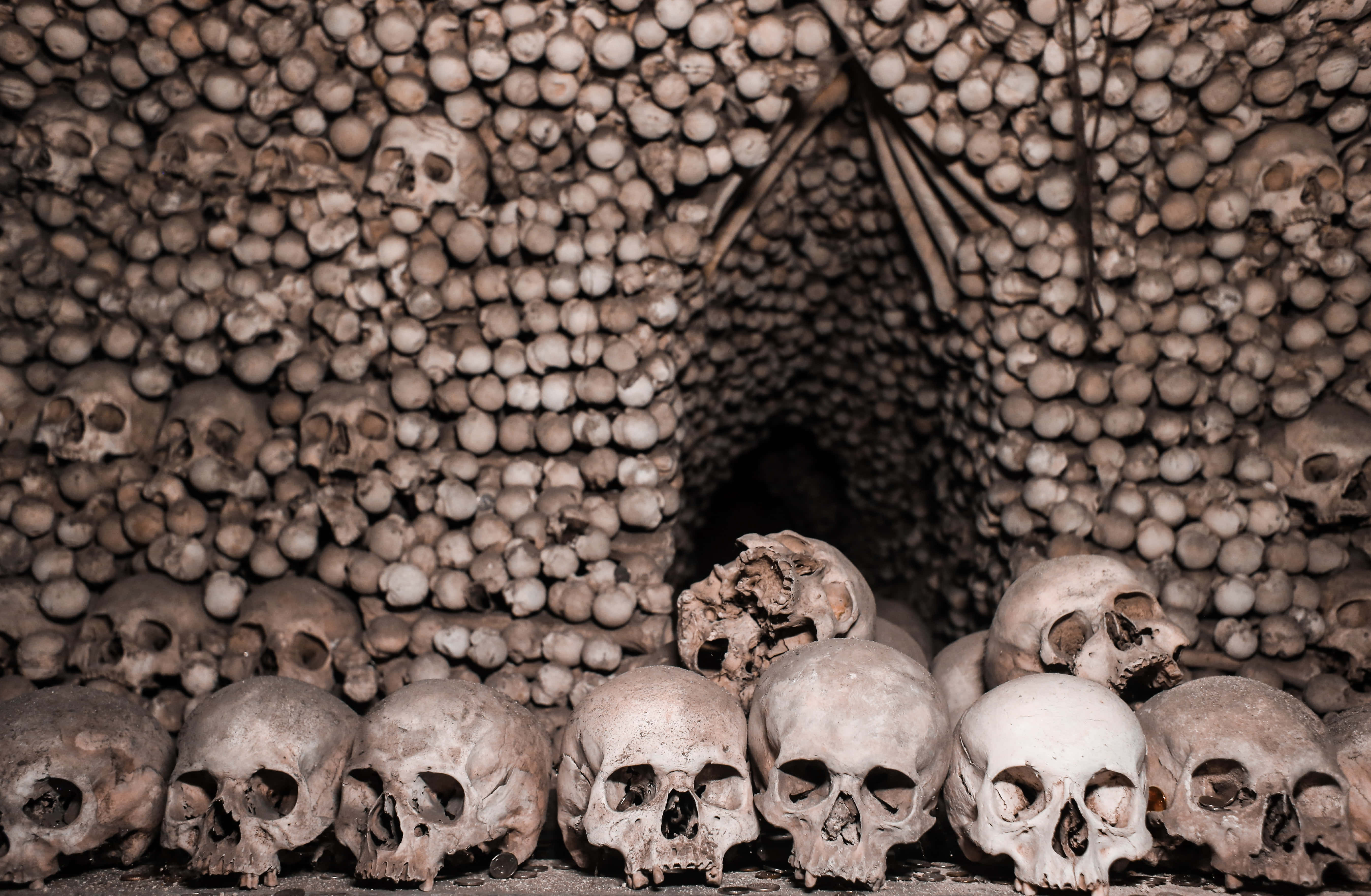 skulls 桌布 壁紙 — 一條令人毛骨悚然的隧道，兩旁堆滿人類頭骨和骨頭，營造出陰沉的藏骨堂氛圍。