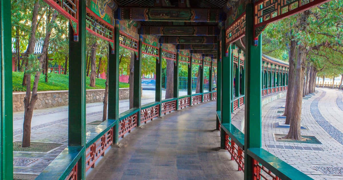 Beijing 桌布 壁紙 — 一條傳統中式亭閣走廊，綠色柱子與紅色欄杆蜿蜒穿過樹木成蔭的花園小徑。