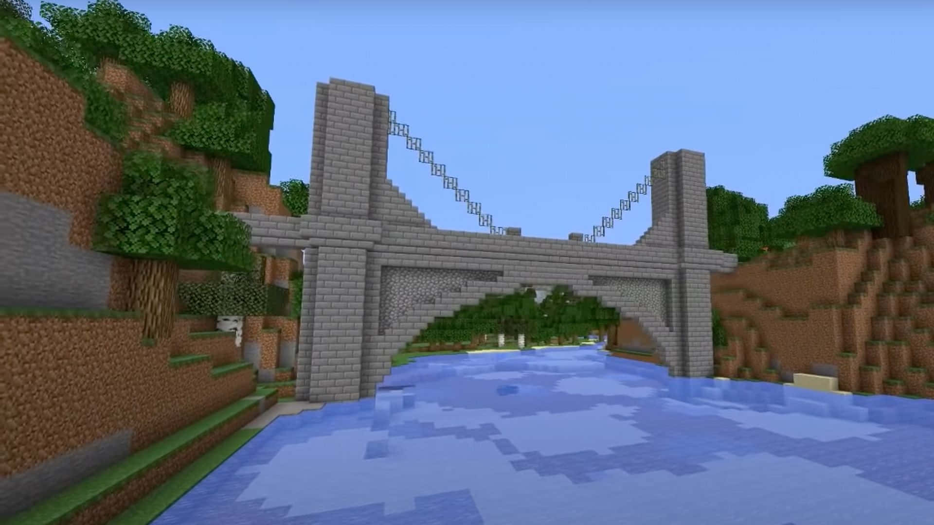 Minecraft Bridges 桌布 壁紙 — 一條像素化的石橋橫跨一條流動的河流，位於方塊狀的Minecraft景觀中，有綠樹和棕色山丘，天空清澈湛藍。