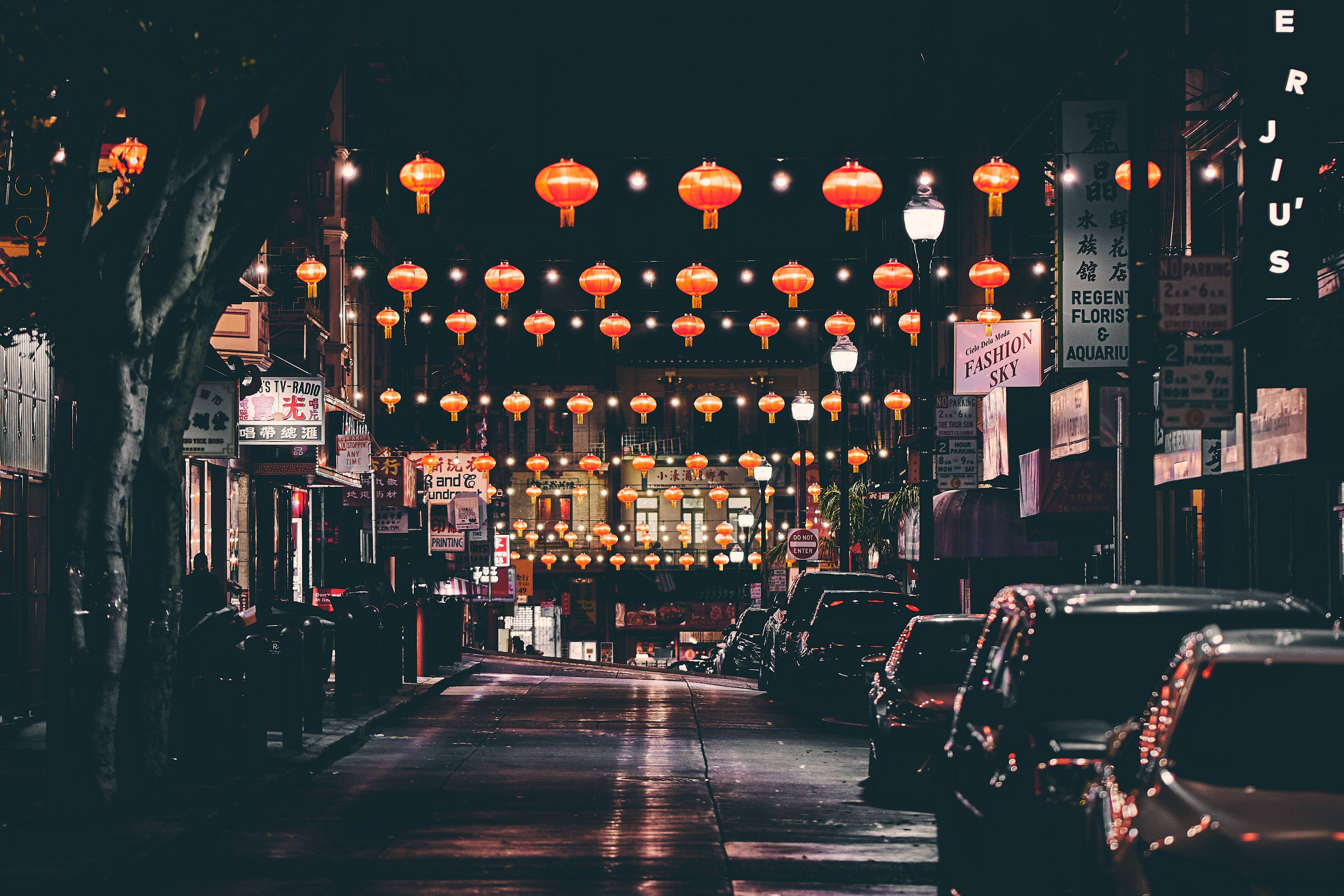 San Francisco 桌布 壁紙 — 一條充滿活力的夜晚街道，裝飾著懸掛在停泊汽車和明亮店面上方的發光紅燈籠。