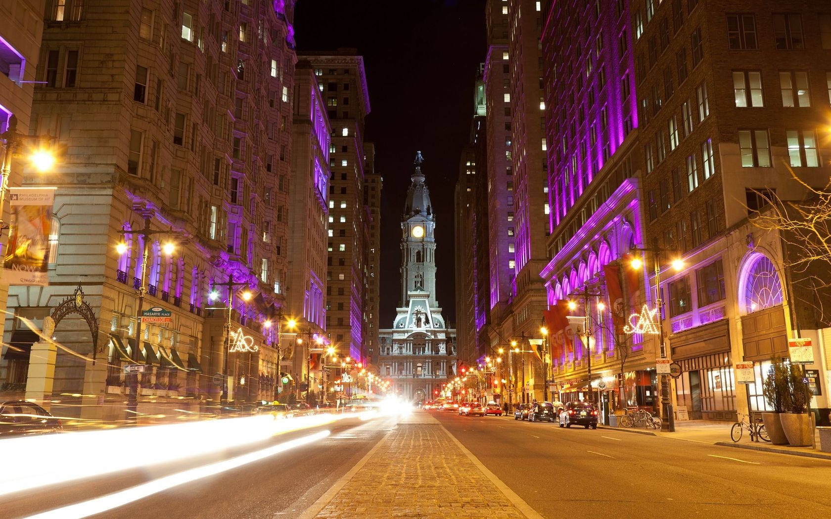 Philadelphia 桌布 壁紙 — 一條充滿活力的夜間城市街道，兩旁是紫色燈光的建築物，盡頭有一座歷史悠久的鐘樓。
